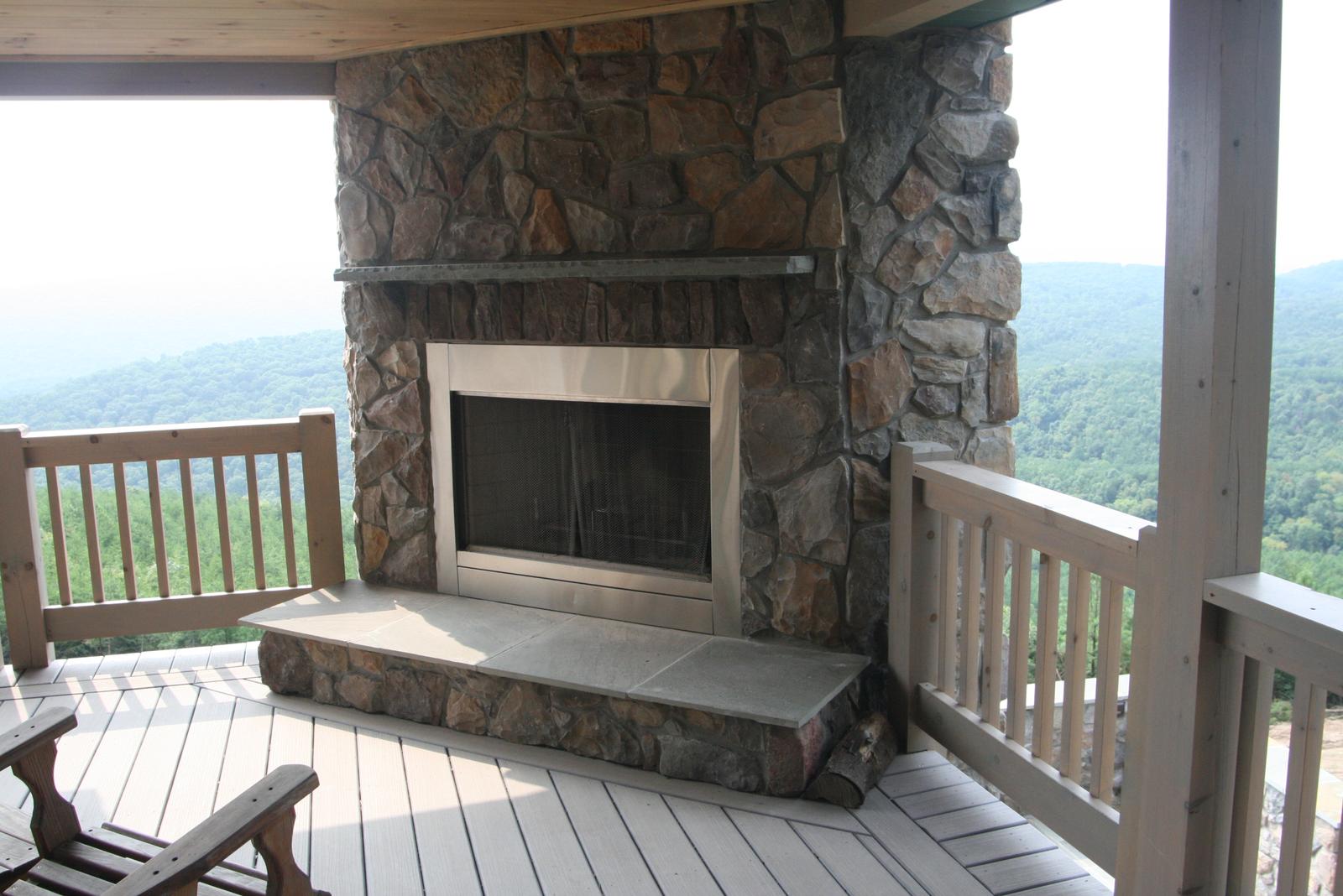 The porch fireplace close to, its stone breast and slab hearth against the open view