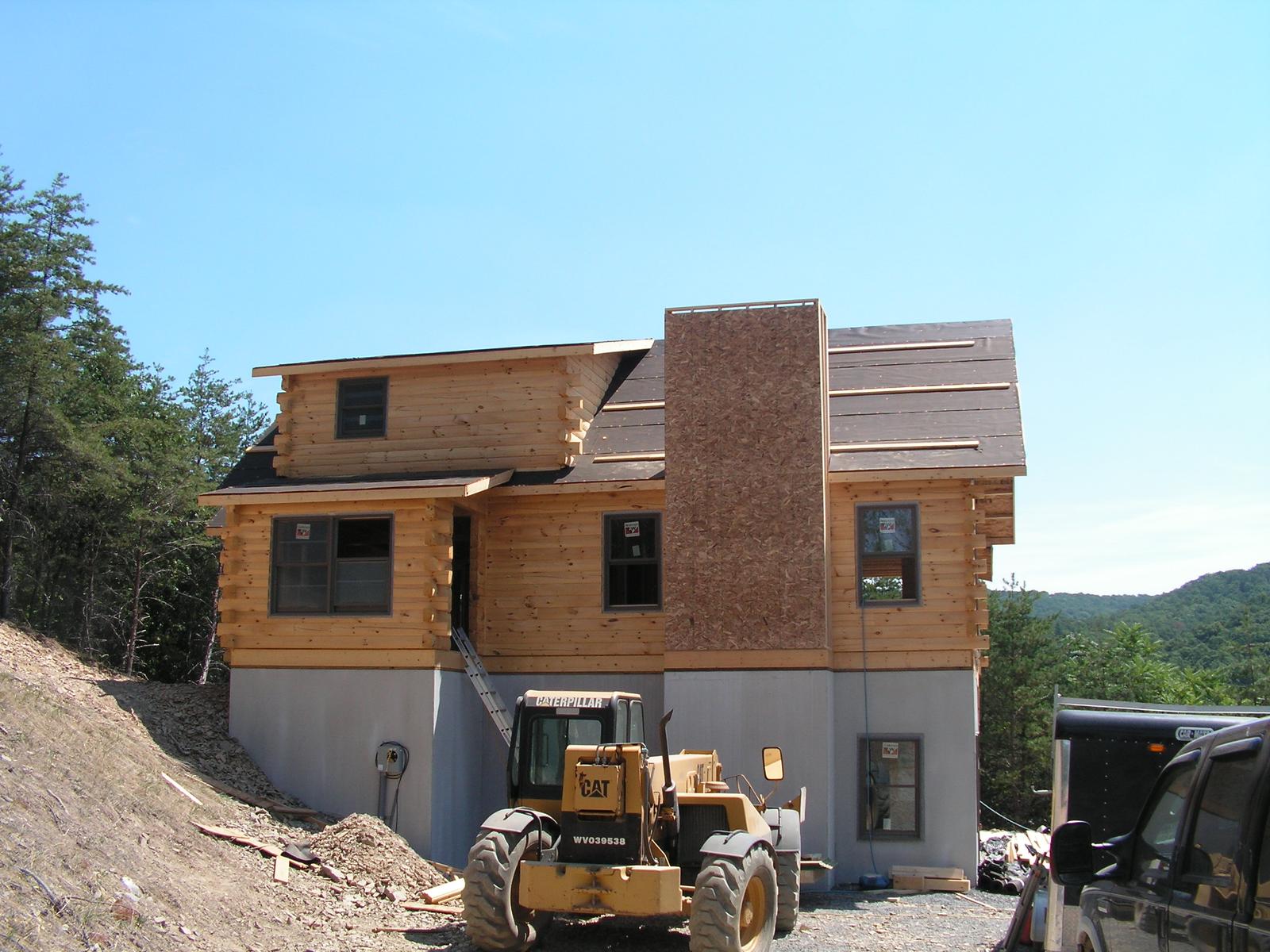A part-clad house with a boxed chimney chase, a loader working on the graded ground in front
