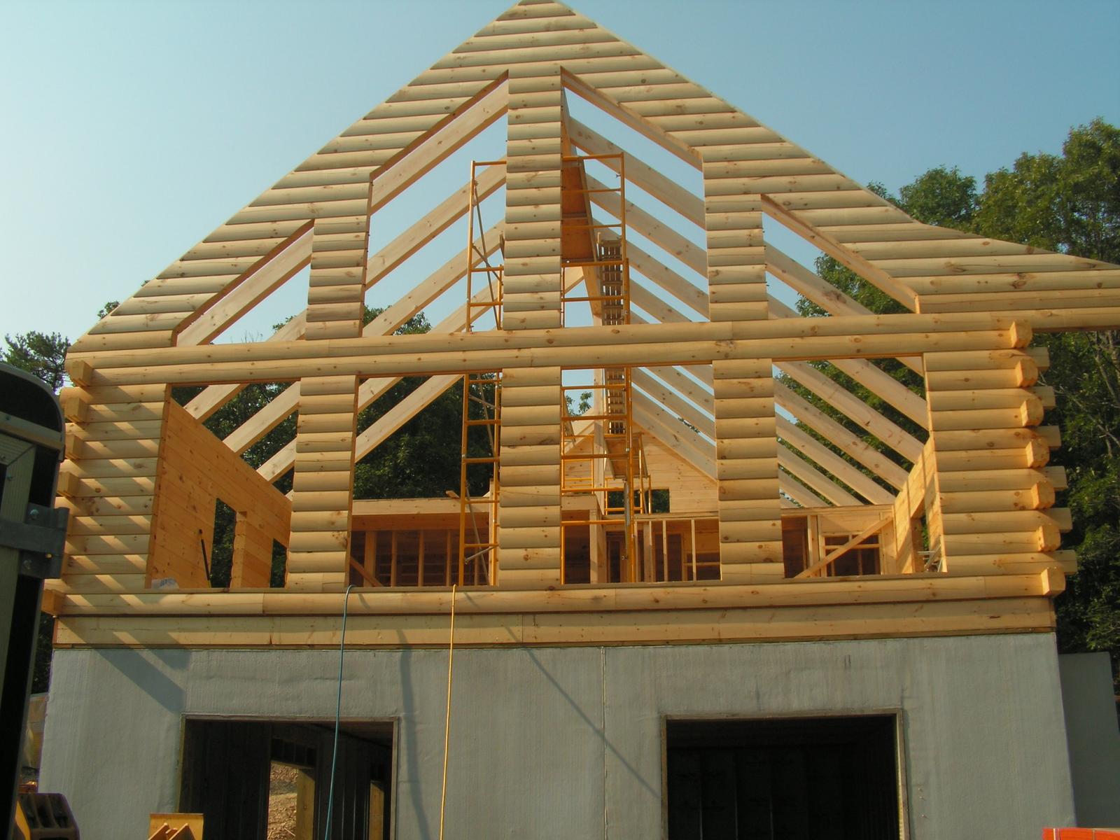 A log gable end raised to full height, its rafter framing open to the sky and a ladder against the wall