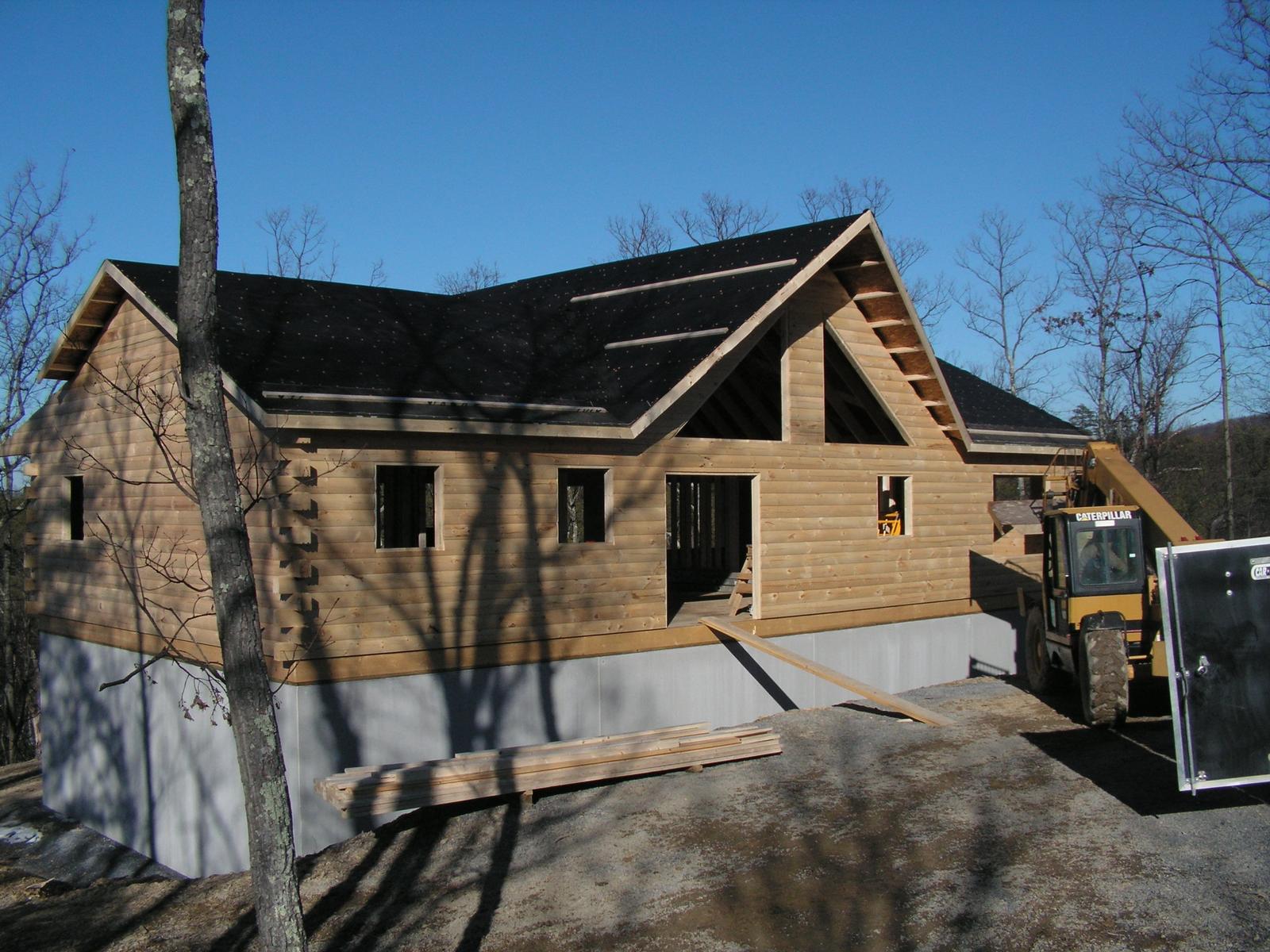 A log home with the roof sheathed and felted, machinery parked close against the wall