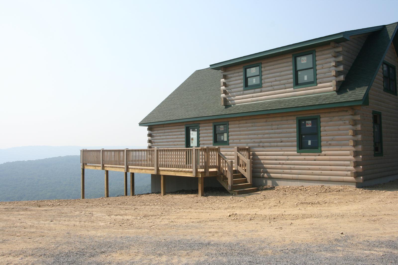 A log home from the open side, its deck standing on posts and the ground falling away to a hazy ridge