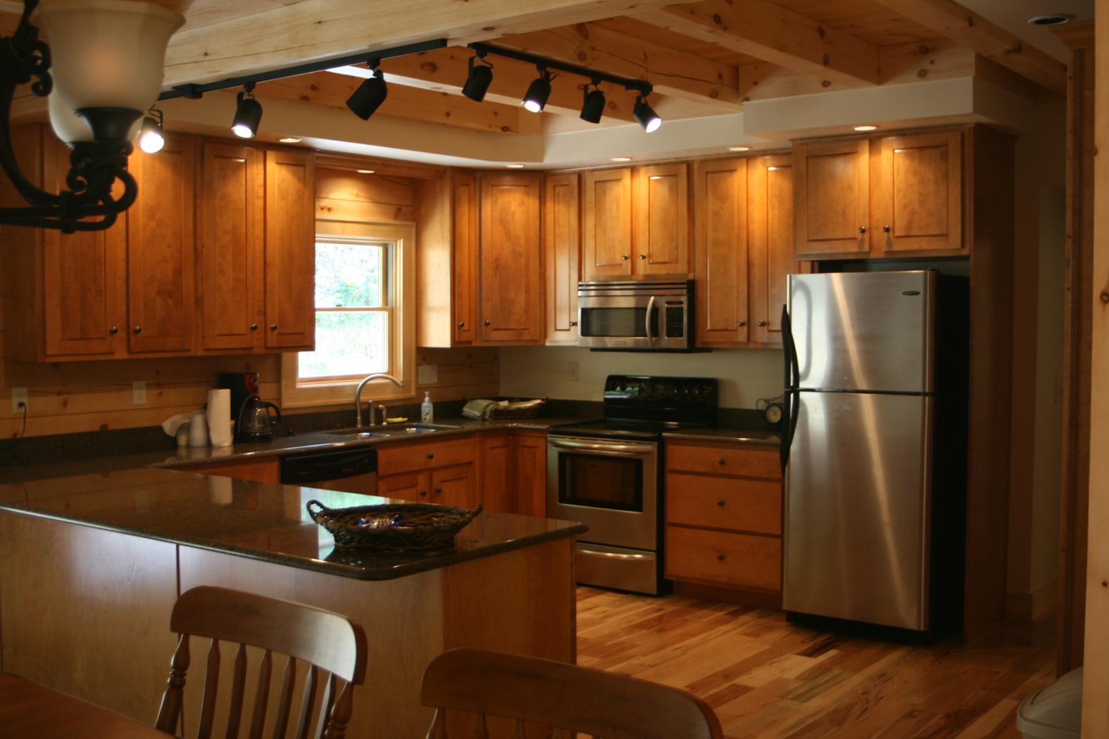A kitchen with wood cabinets and a stone counter, stainless range and refrigerator under track lighting