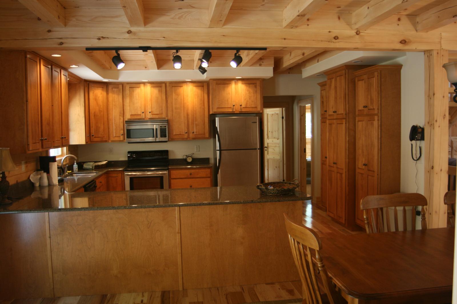 The kitchen from the dining end, exposed beams overhead and a breakfast bar with chairs drawn up