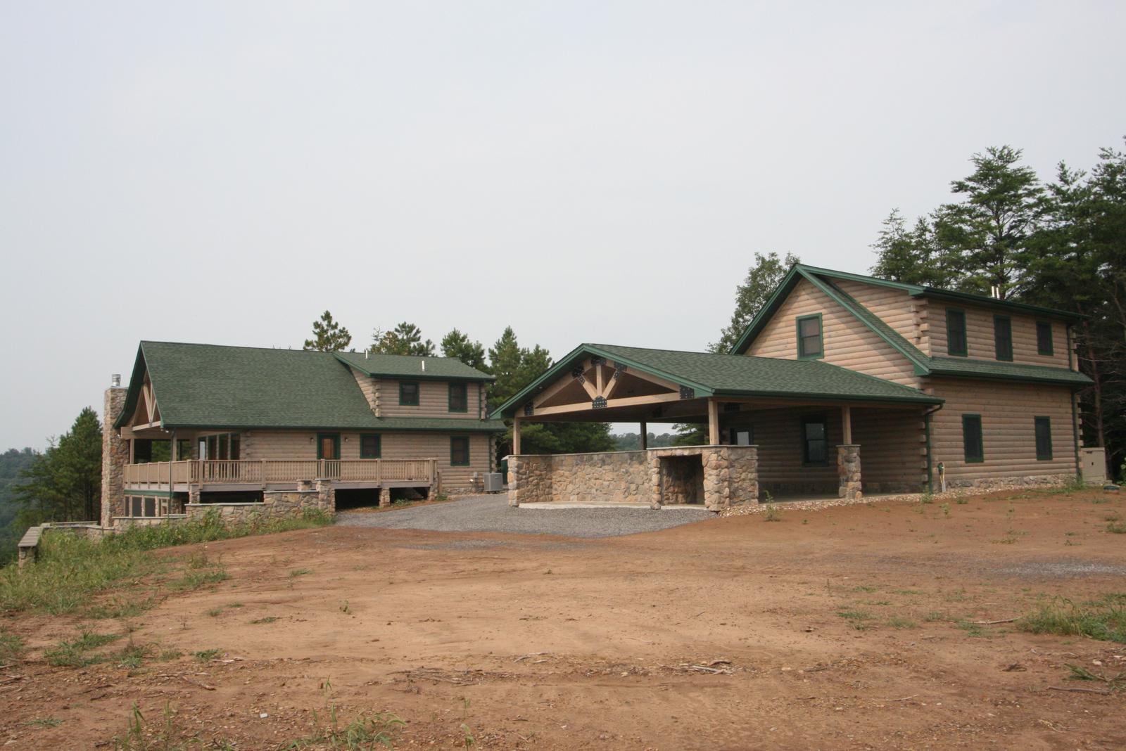 Two buildings on a cleared site, a house with a green roof and a matching detached garage joined by a gravel drive