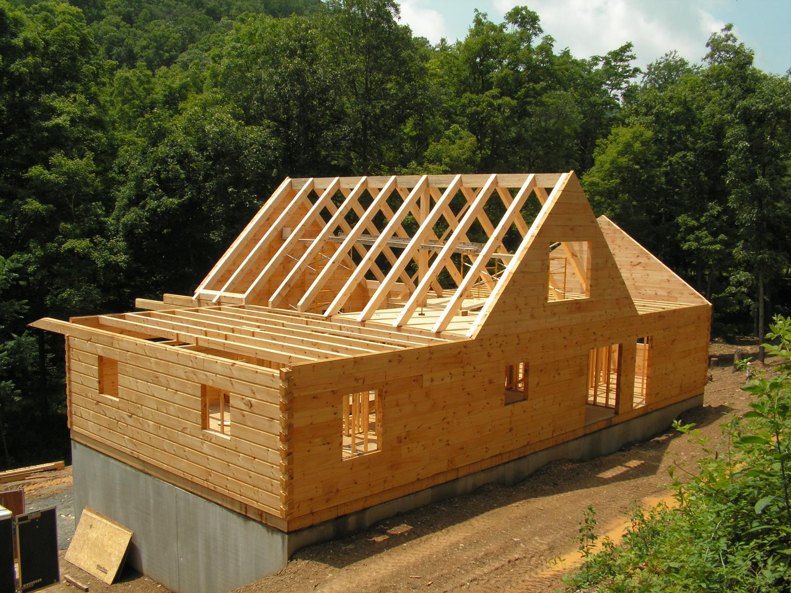 Roof rafters being set over stacked log walls, the sheathing started at one end