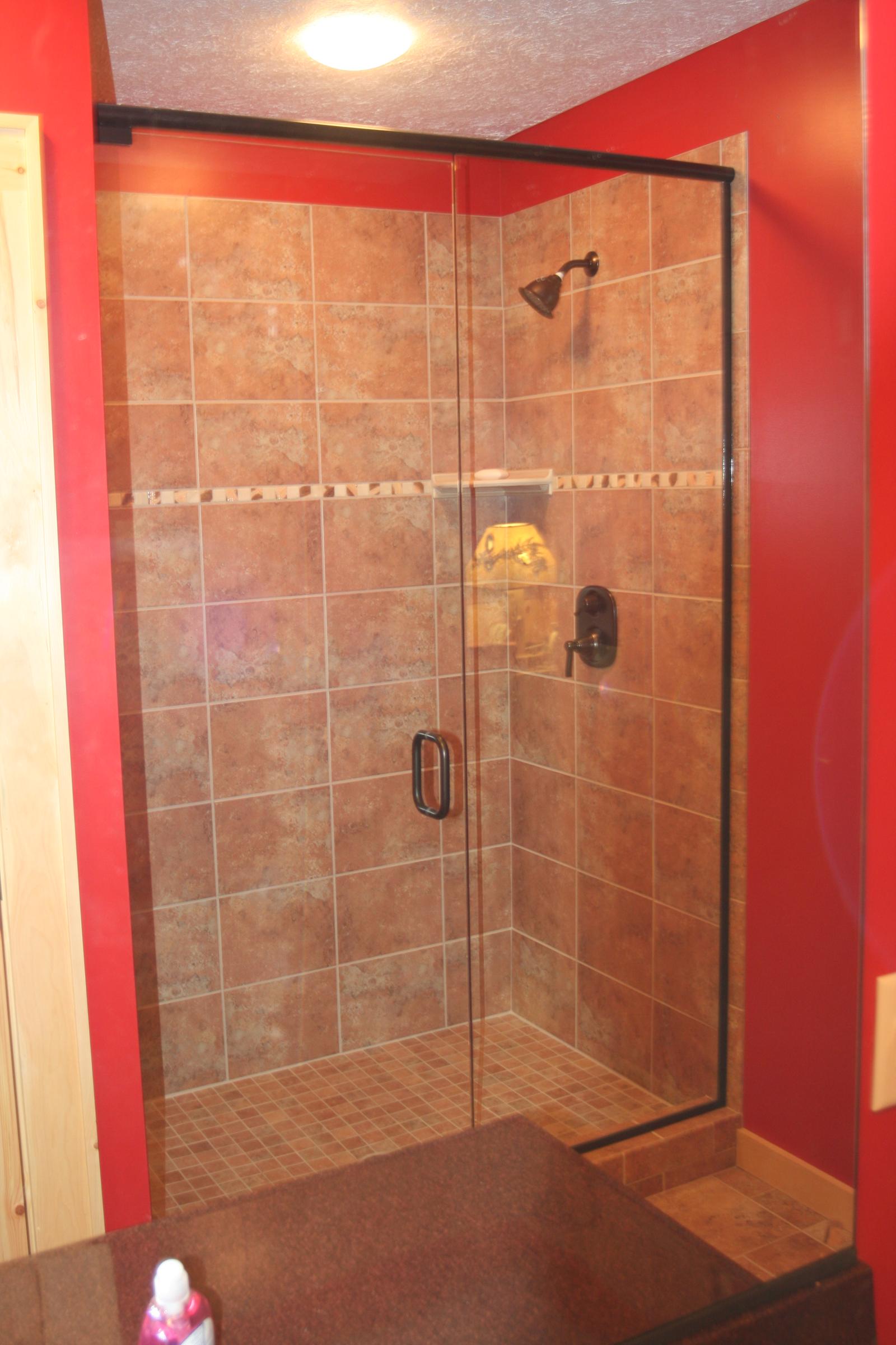 A tiled shower with a glass door and a corner seat, a decorative tile band at shoulder height, red painted walls either side