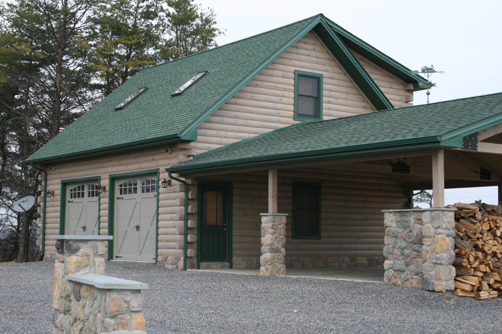 A detached garage with two carriage doors and roof skylights, a covered bay beside it on stone piers stacked deep with split firewood