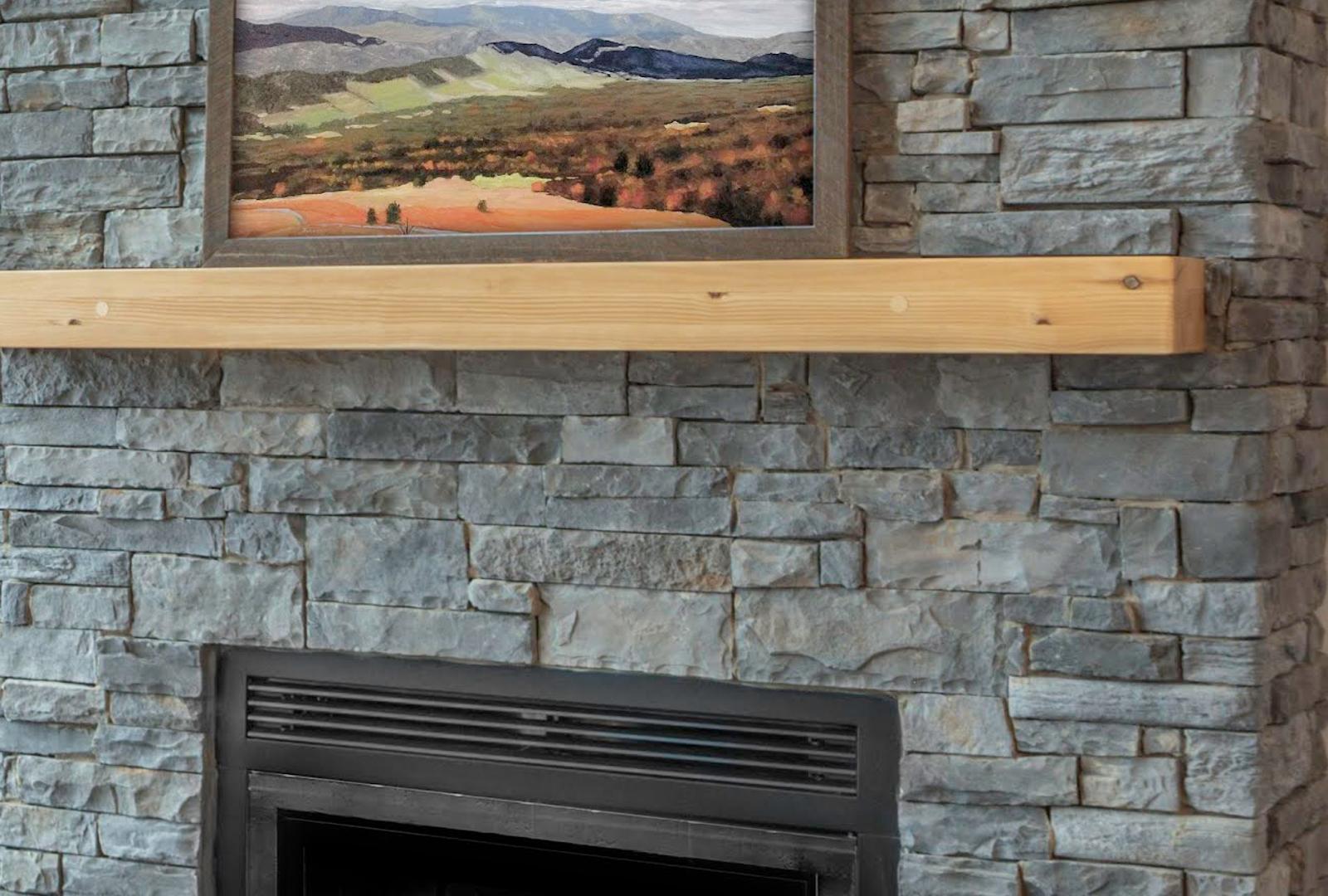 Close view of a gray dry-stacked ledgestone chimney breast in tight thin horizontal courses, a squared light timber mantel spanning it, the stone returning around a corner on the right