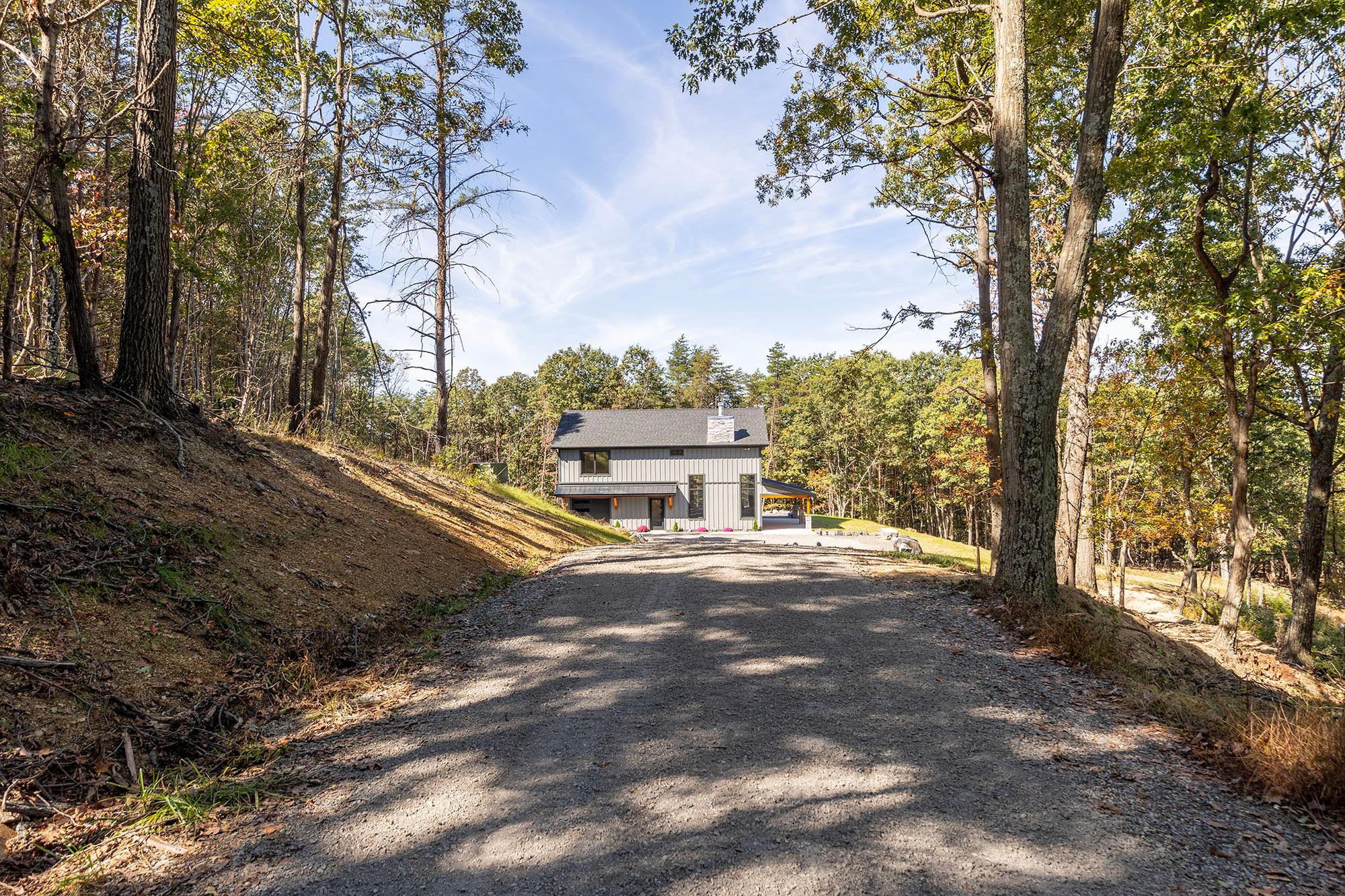 The home at the top of its gravel drive with flowers at the entries, seen from the tree-lined approach