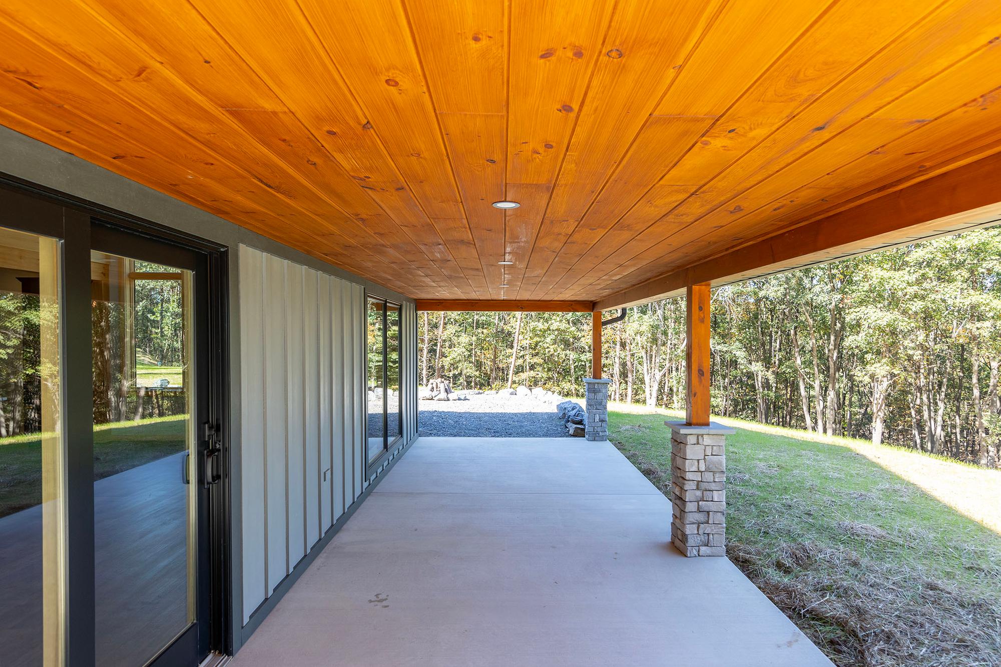 Covered patio with a pine plank ceiling, recessed lights, stone-clad pier columns and a sliding glass door into the house