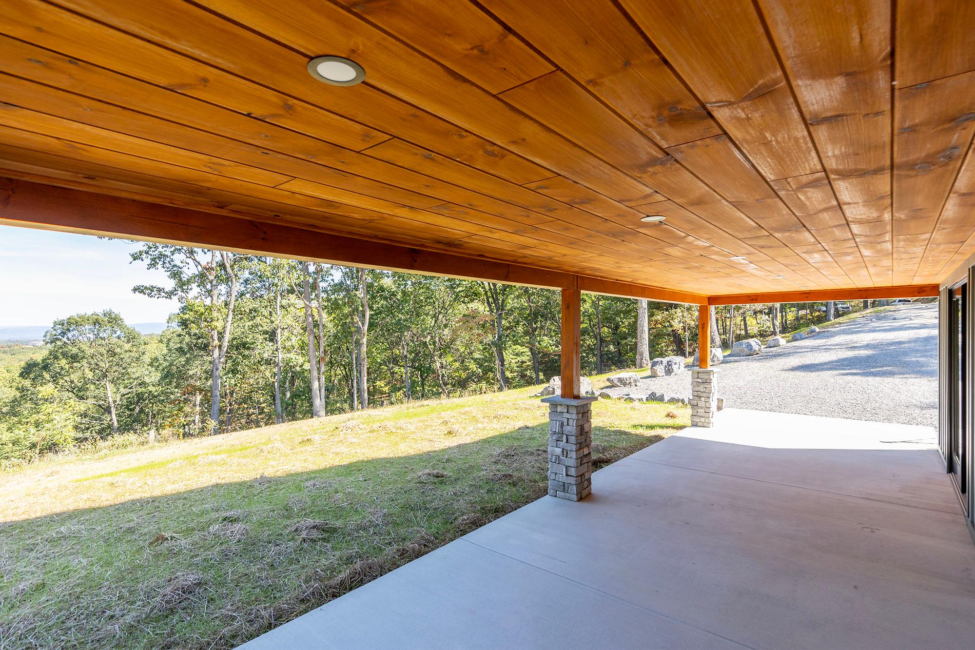 Corner of the covered patio looking past stone piers to the gravel drive and a hazy ridge on the horizon