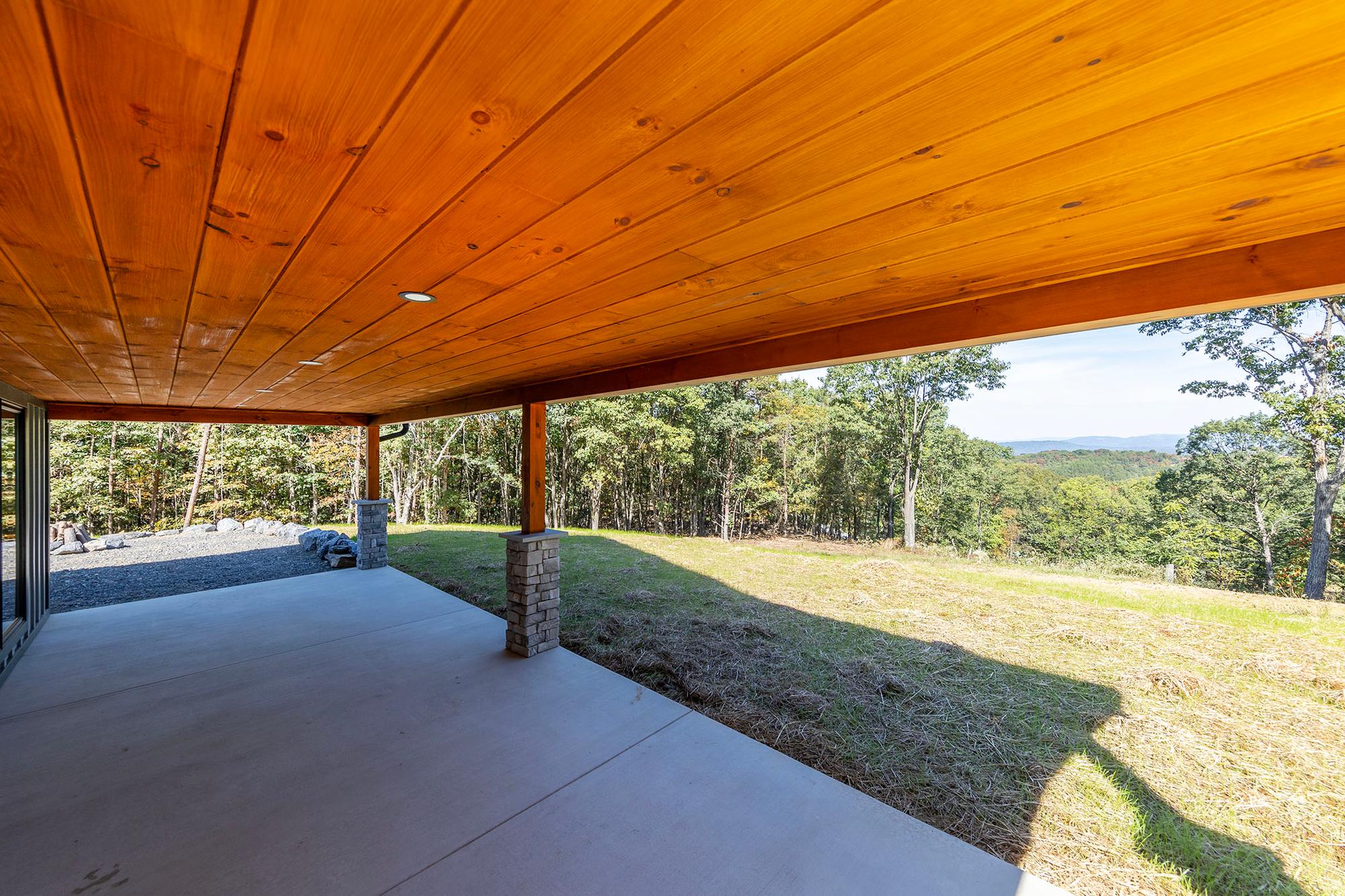 View from under the covered patio across a grass slope to forested ridges in the distance