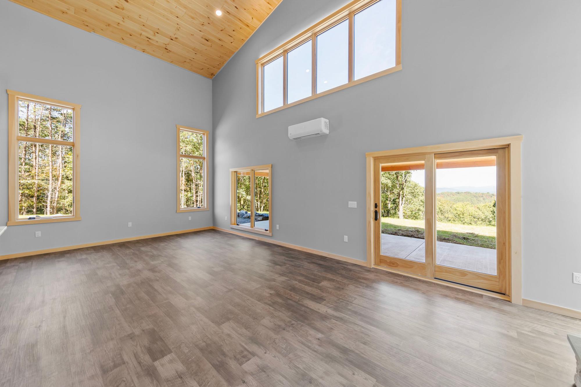 Empty great room corner with a clerestory window band, wall-mounted mini-split, and a sliding glass door to the patio and lawn