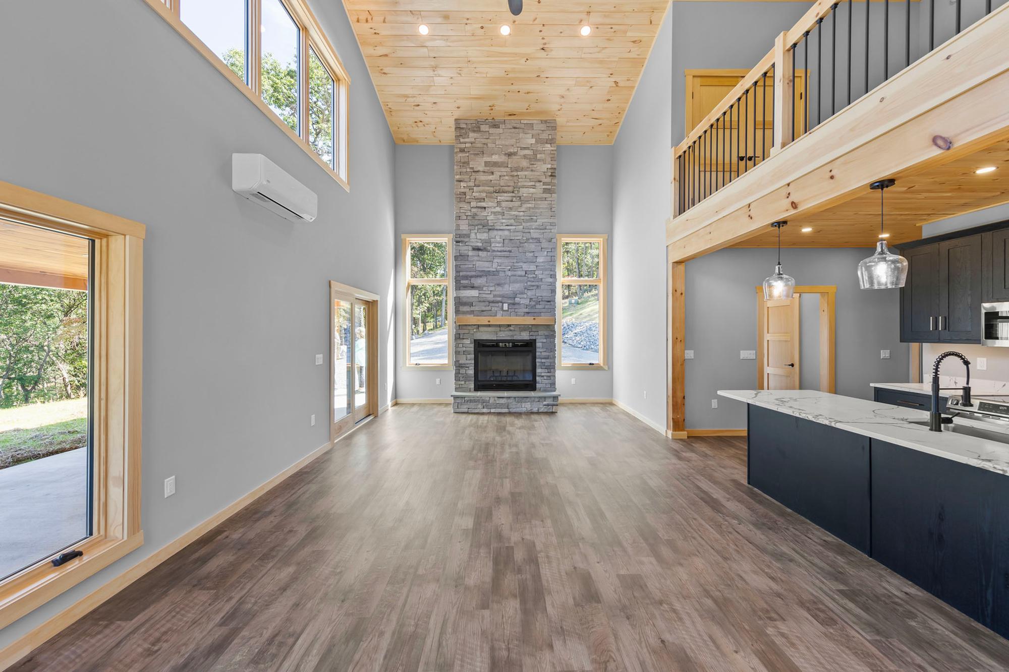 Floor-to-ceiling stacked-stone fireplace between two windows in the unfurnished great room, the kitchen island to the right