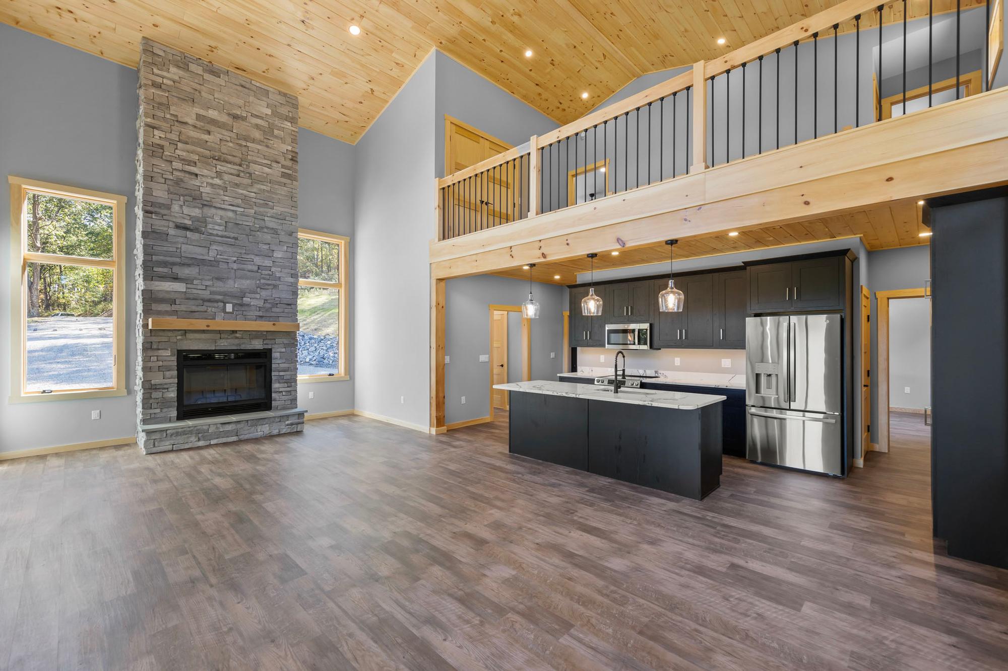 Unfurnished great room showing the stone chimney, kitchen with stainless appliances, and windows onto the gravel drive
