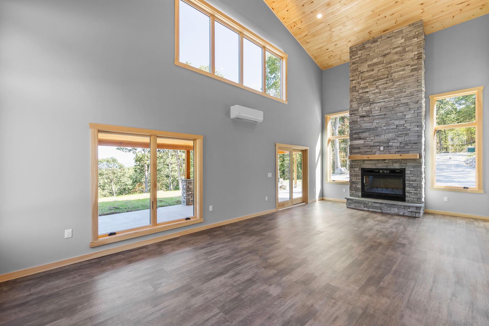 Stone fireplace with a wood mantel under clerestory windows, a mini-split on the wall and glass doors reflecting the patio