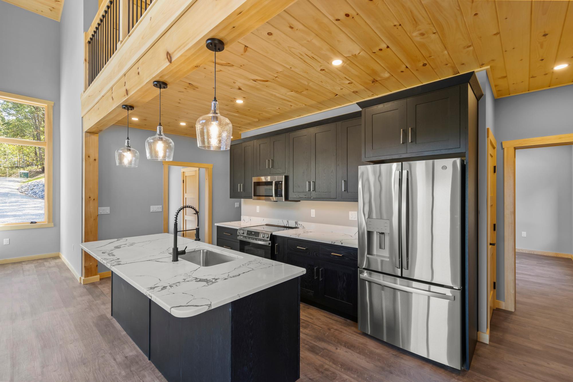 Kitchen with dark cabinets, marble-look island, glass pendants and stainless appliances beneath the pine loft beam