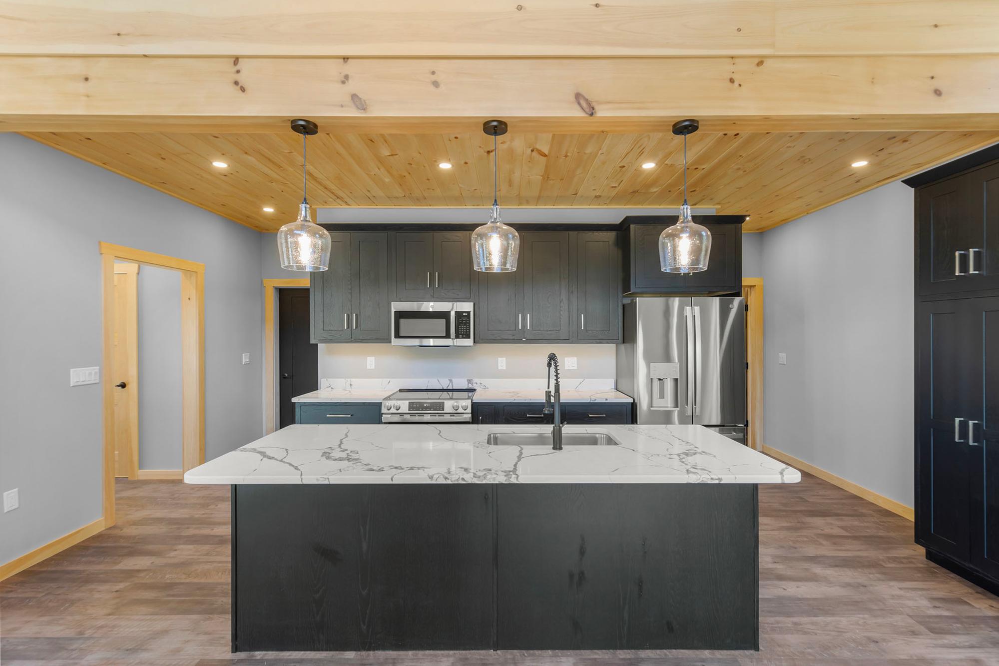 Kitchen elevation with three glass pendants over the island sink, dark cabinets, and a stainless French-door refrigerator