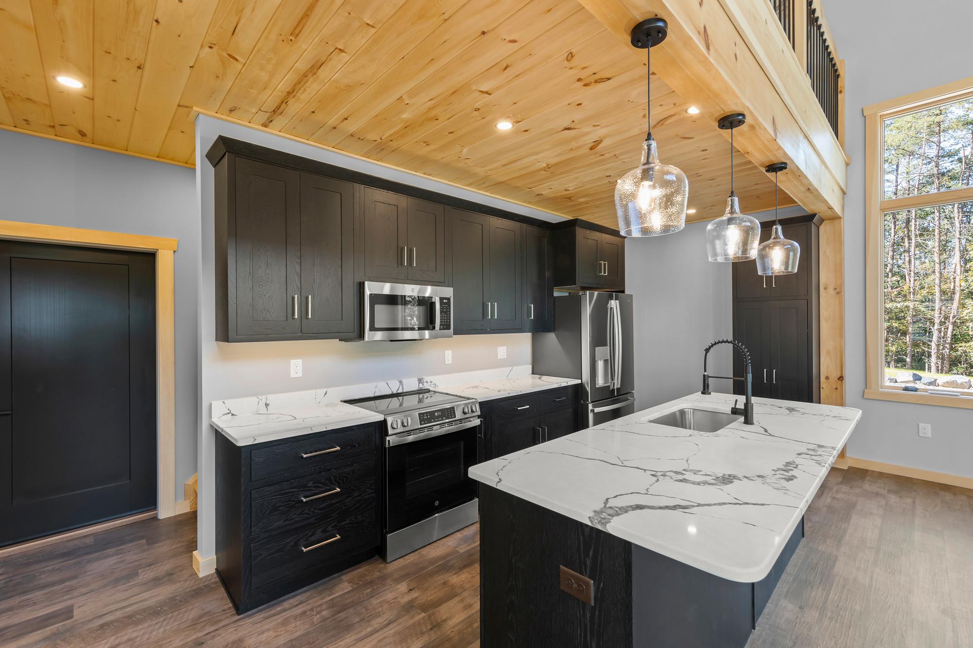 Kitchen corner with a stainless range and microwave, marble-look counters, and a window into the pines
