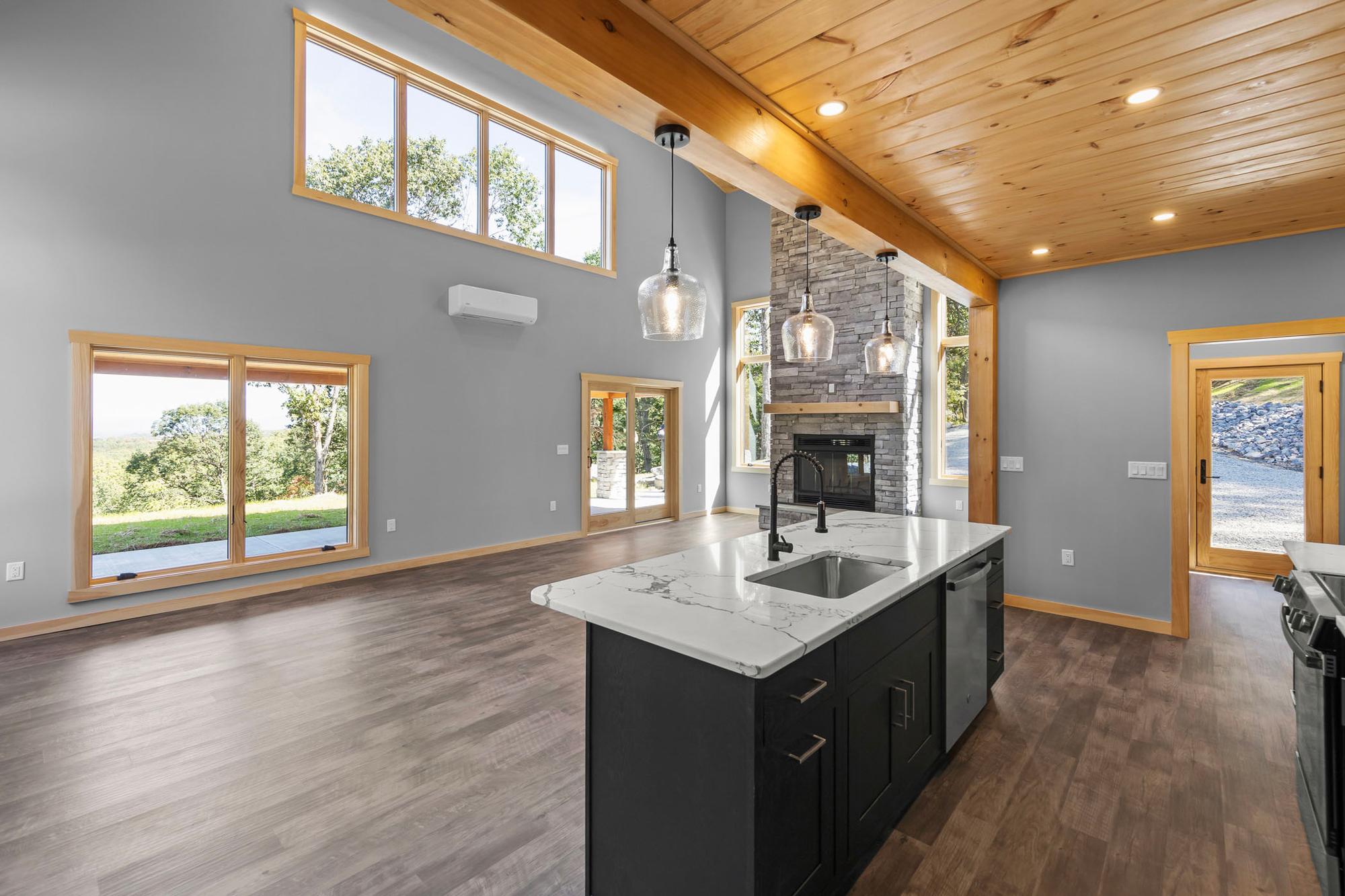 Kitchen island in the foreground with the stacked-stone fireplace beyond and windows onto the covered patio and lawn
