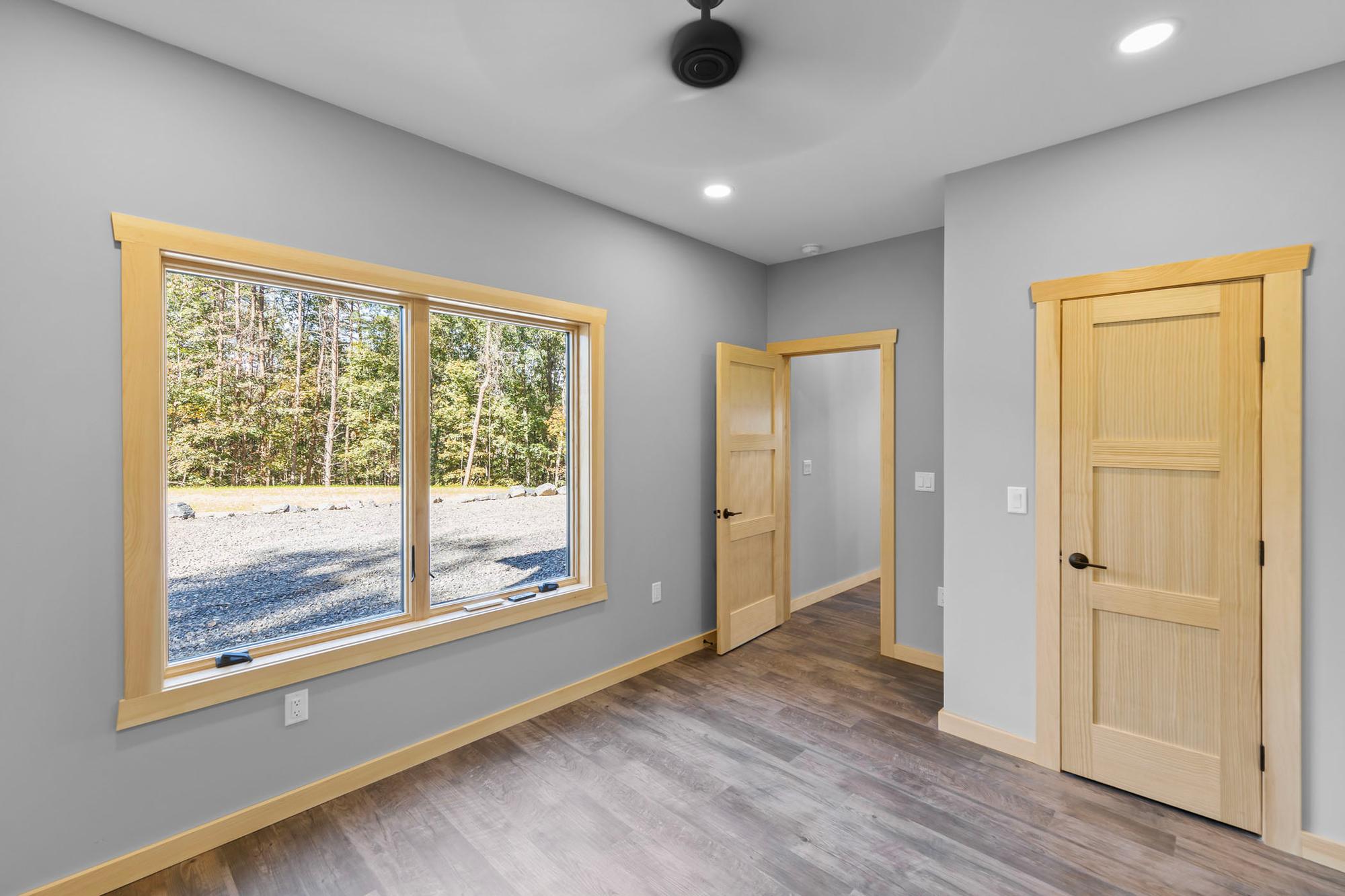 Unfurnished bedroom with a wide window facing the gravel clearing, pine doors to the hall and closet, and a ceiling fan