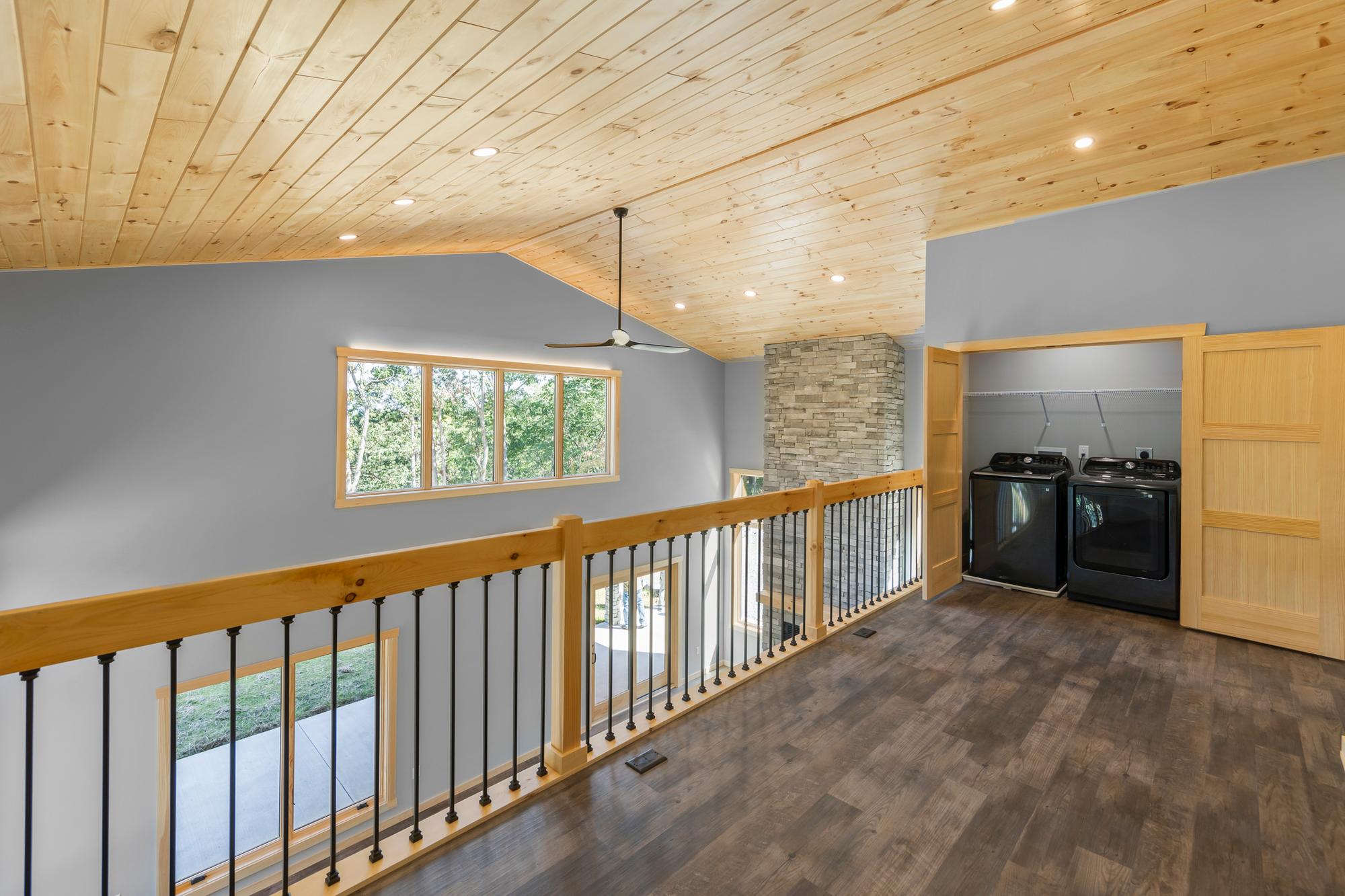 Loft with a black washer and dryer in an open alcove beside the stacked-stone chimney and a sliding pine door