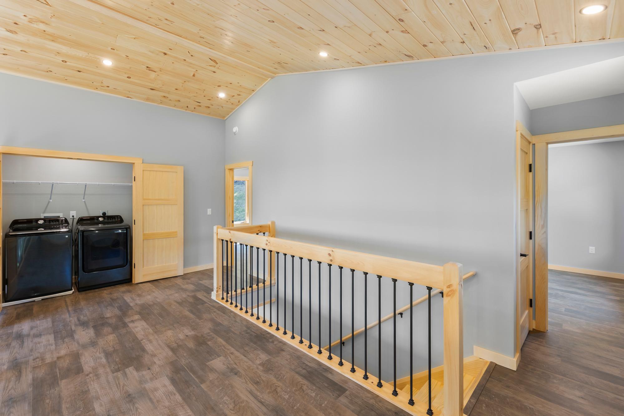 Upstairs landing with an open laundry closet holding a black washer and dryer, next to the timber stair railing