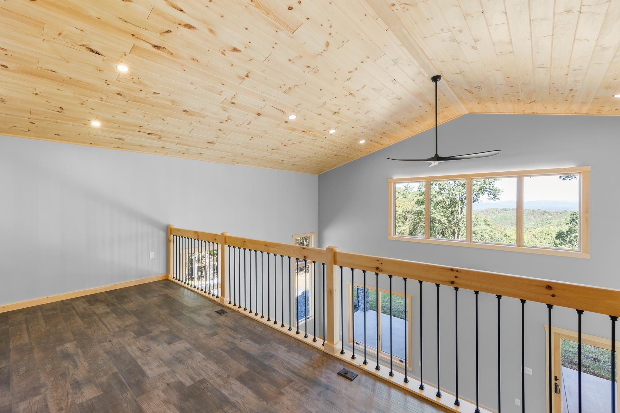 Empty loft with a picture window framing a long ridge view, a black ceiling fan and railing overlooking the great room
