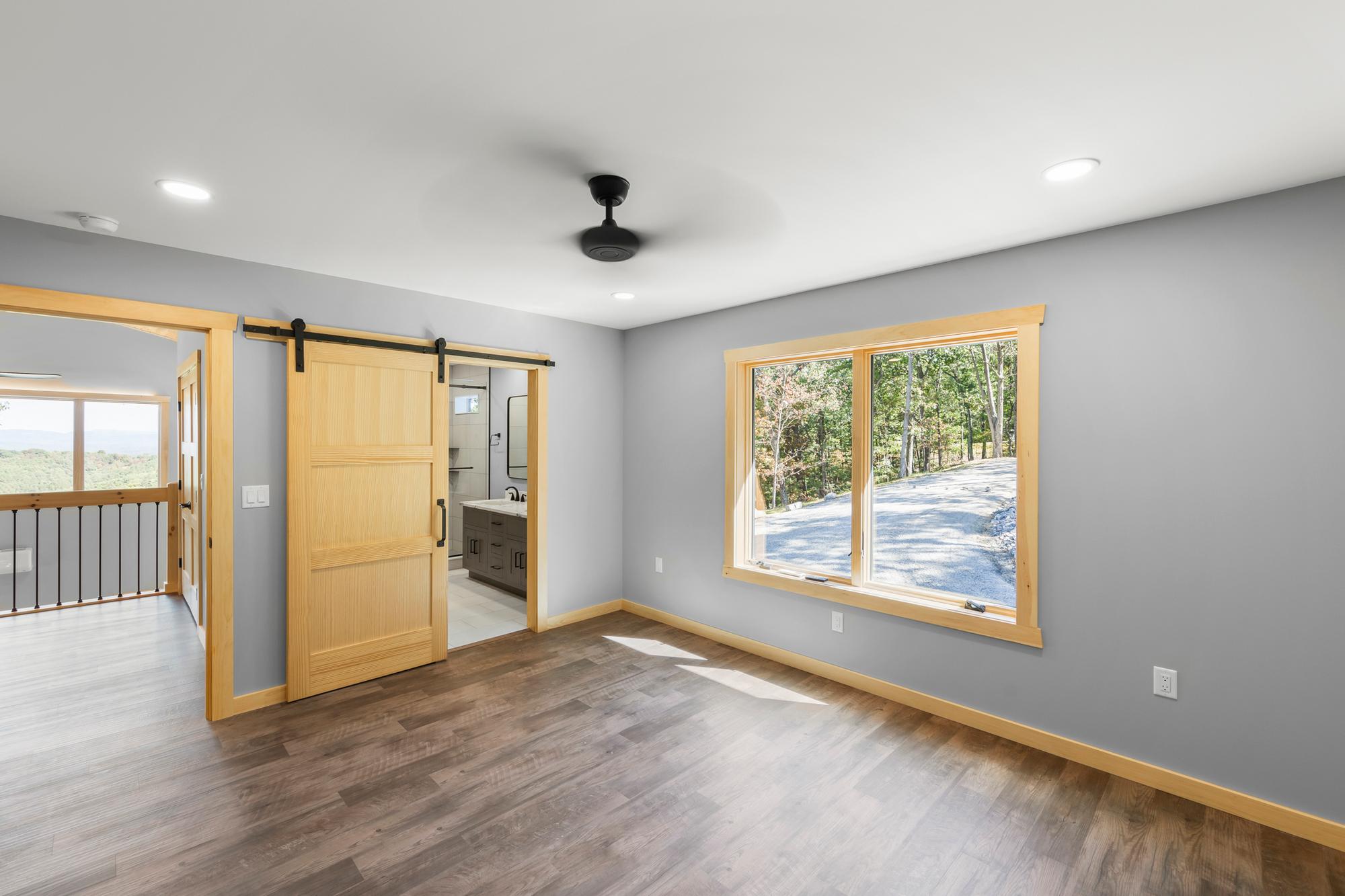 Bedroom with a sliding pine barn door open to its bathroom vanity, and a window onto the gravel drive