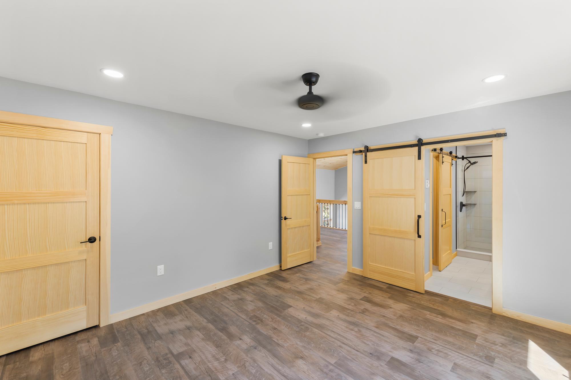 Bedroom corner with an open pine door toward the loft and a sliding barn door revealing the tiled walk-in shower