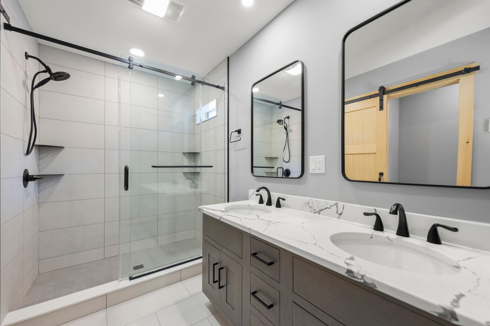Bathroom with a dark-wood double vanity, marble-look top, two black-framed mirrors and a glass-doored tile shower