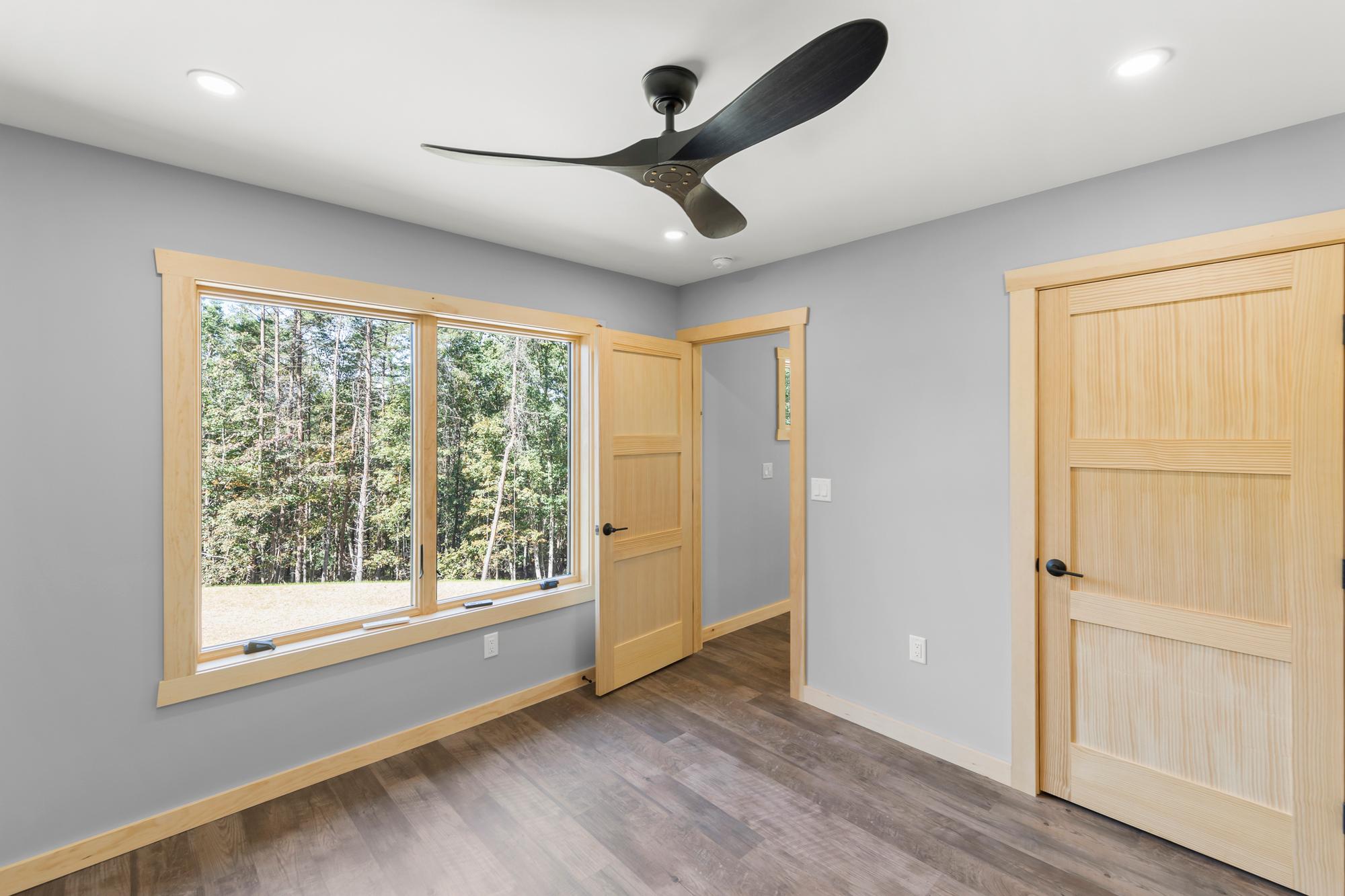 Unfurnished bedroom with a ceiling fan and a wide pine-trimmed window onto the field at the wood's edge