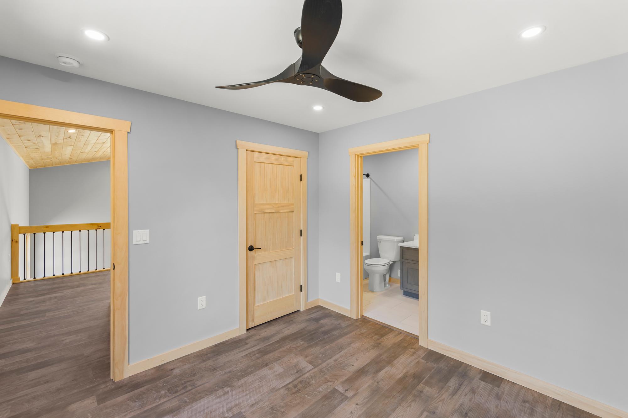 Bedroom with its own bathroom — toilet and gray vanity seen through the doorway — and the loft railing visible down the hall