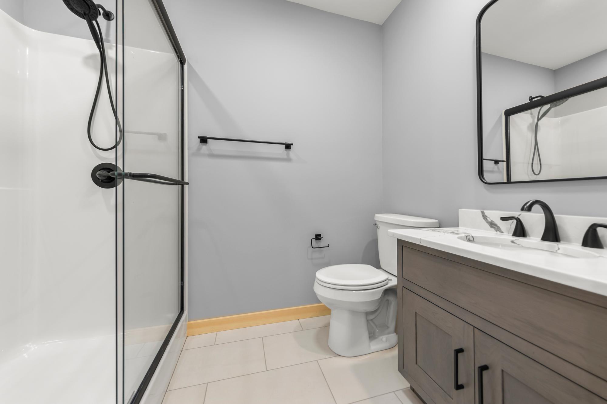 Bathroom with a glass-doored fiberglass shower, black fixtures, toilet, and gray vanity below a black-framed mirror