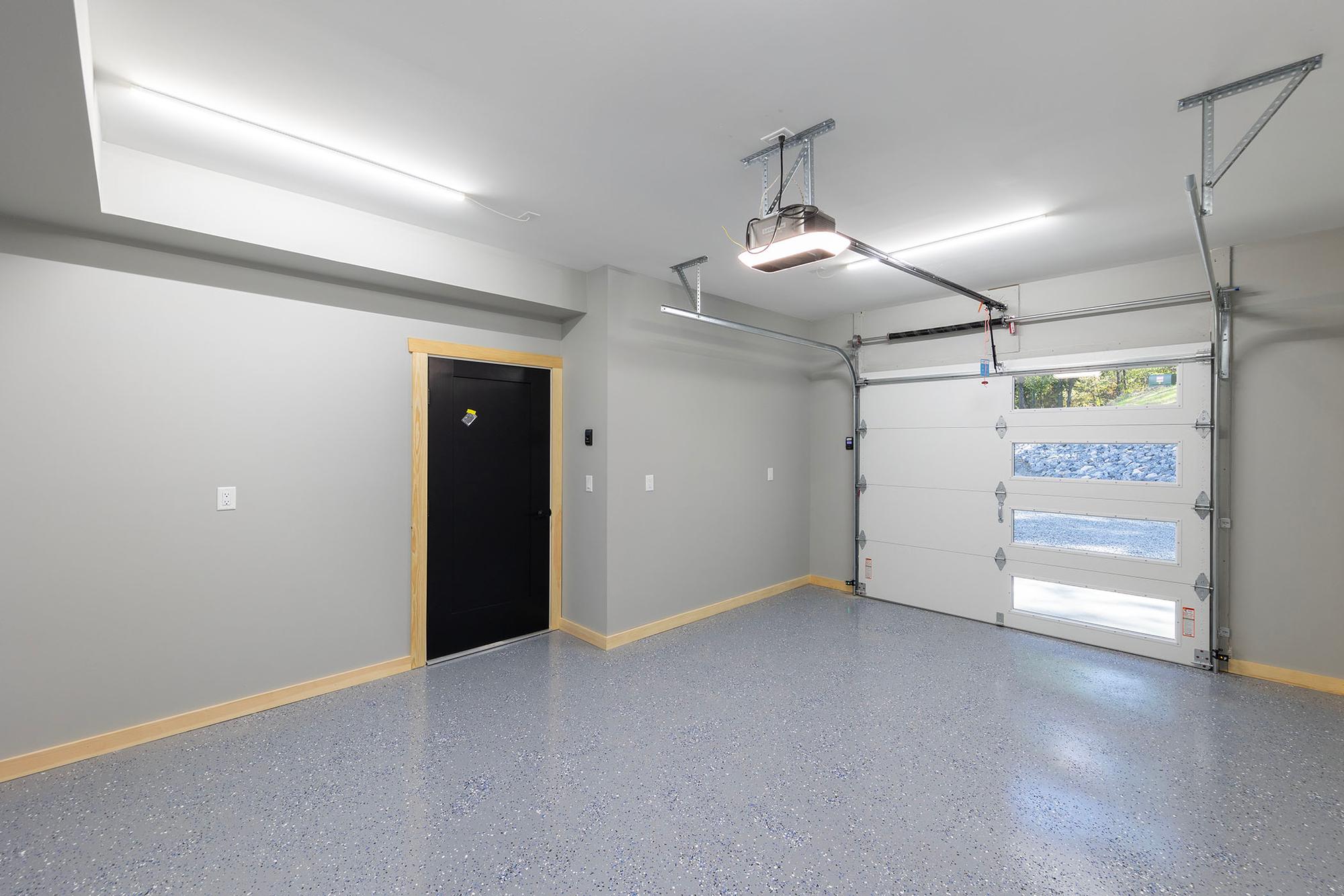 Garage interior with a speckled epoxy floor, a white insulated door with window lites onto the rock bank, and a black entry door