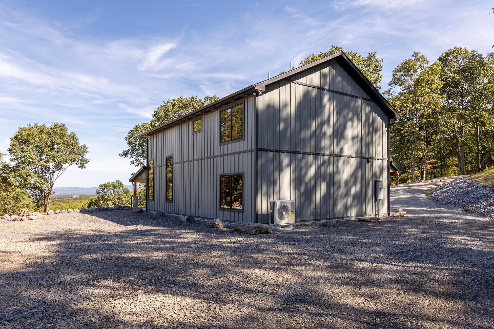 Rear corner of the home with board-and-batten siding, a ductless mini-split unit at the foundation, and a valley view beyond the gravel drive