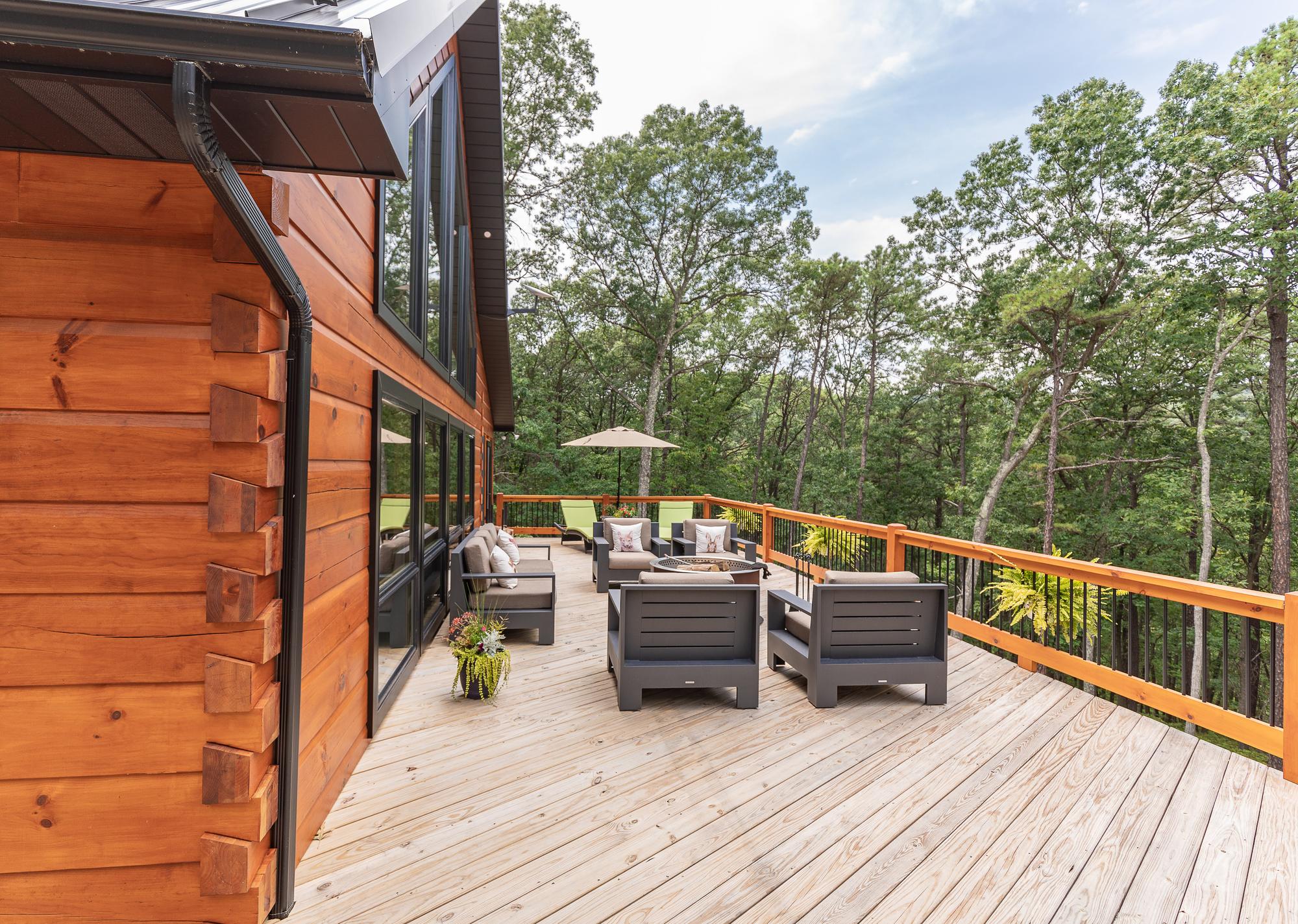 Deck corner with an outdoor sofa, loungers and a market umbrella against dense forest