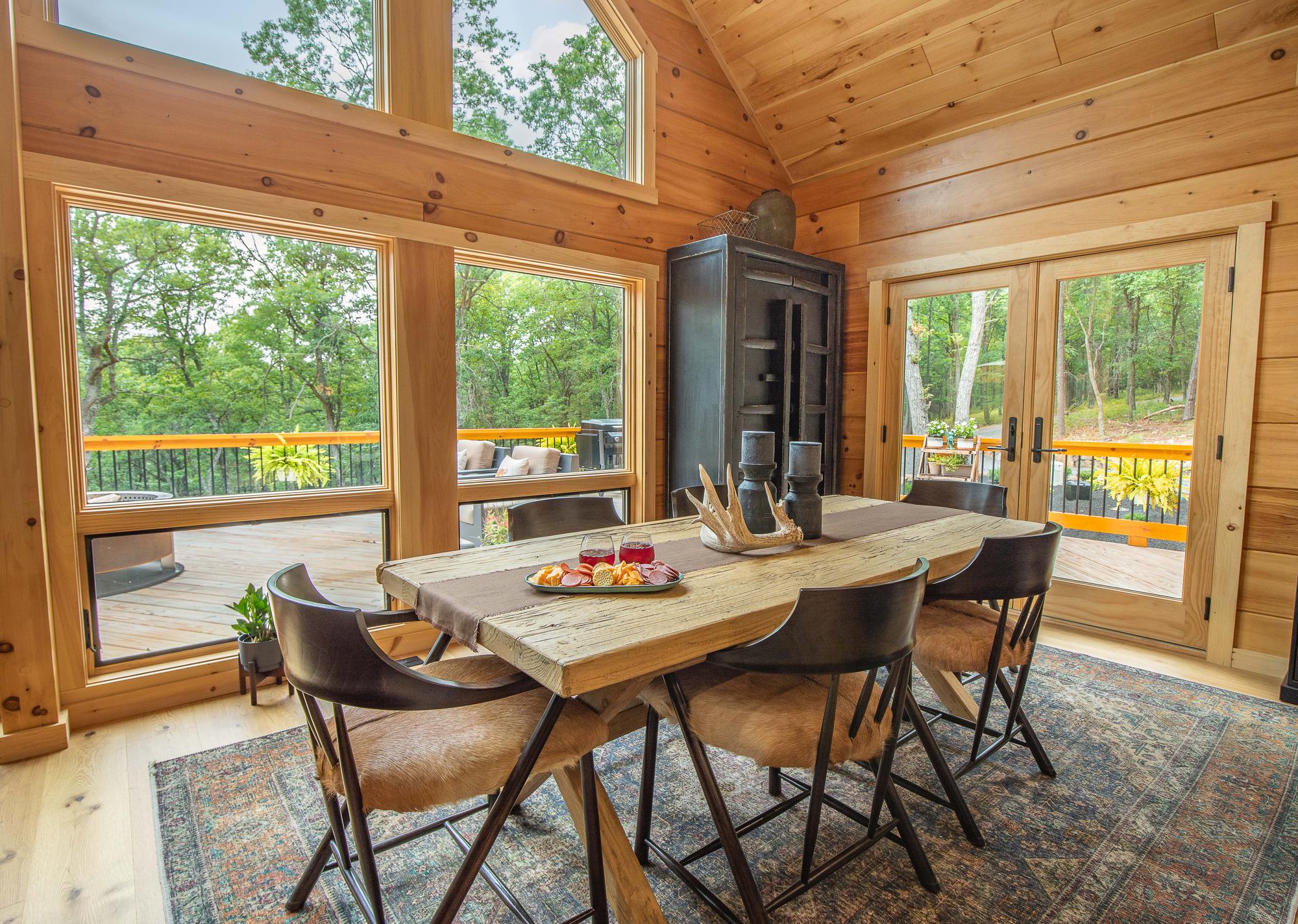 Dining area with a live-edge table beneath a vaulted ceiling and a wall of windows onto the forest