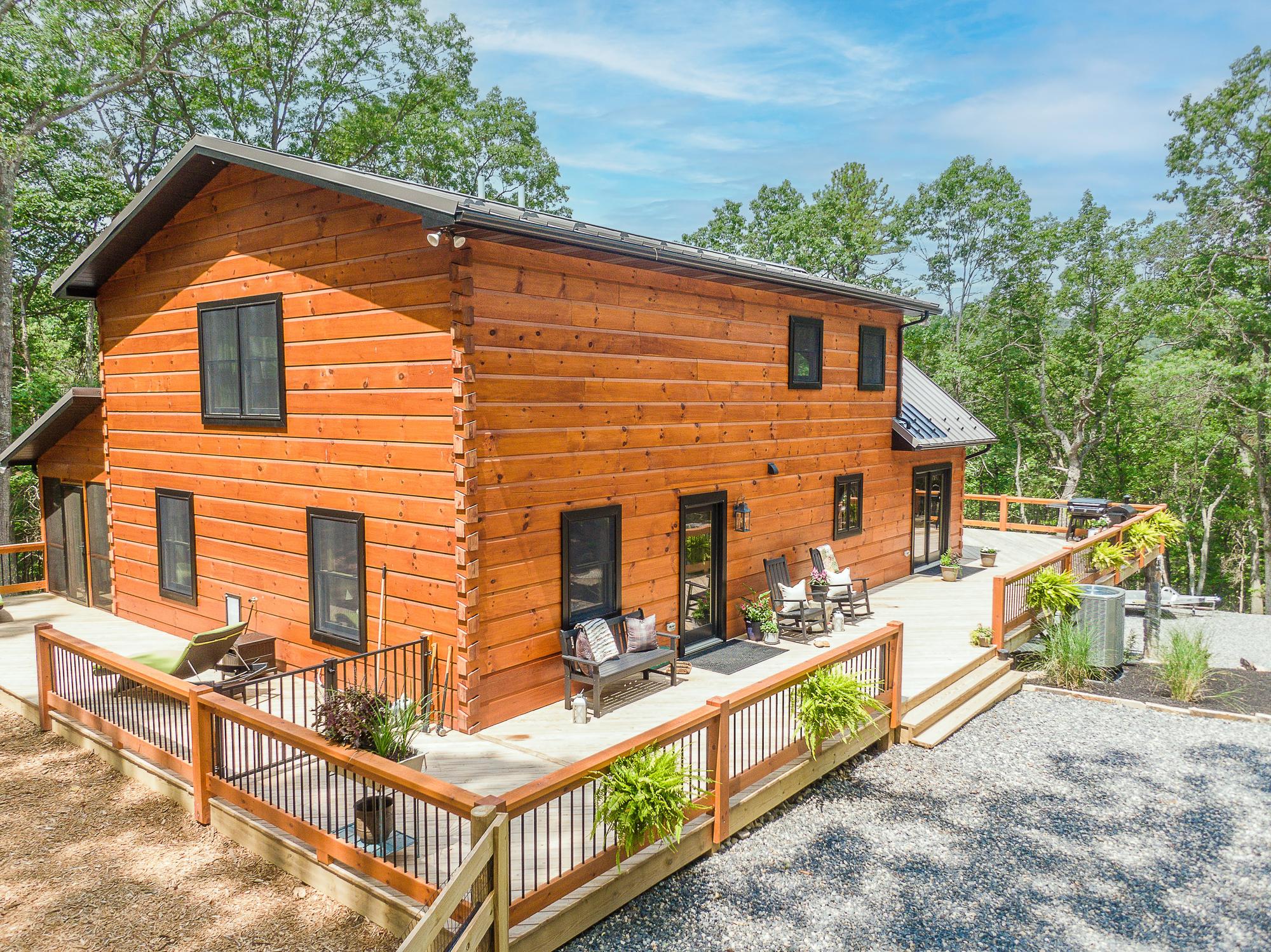 The gable end of the log home seen from above, its concrete patio enclosed by a wood rail with black metal balusters
