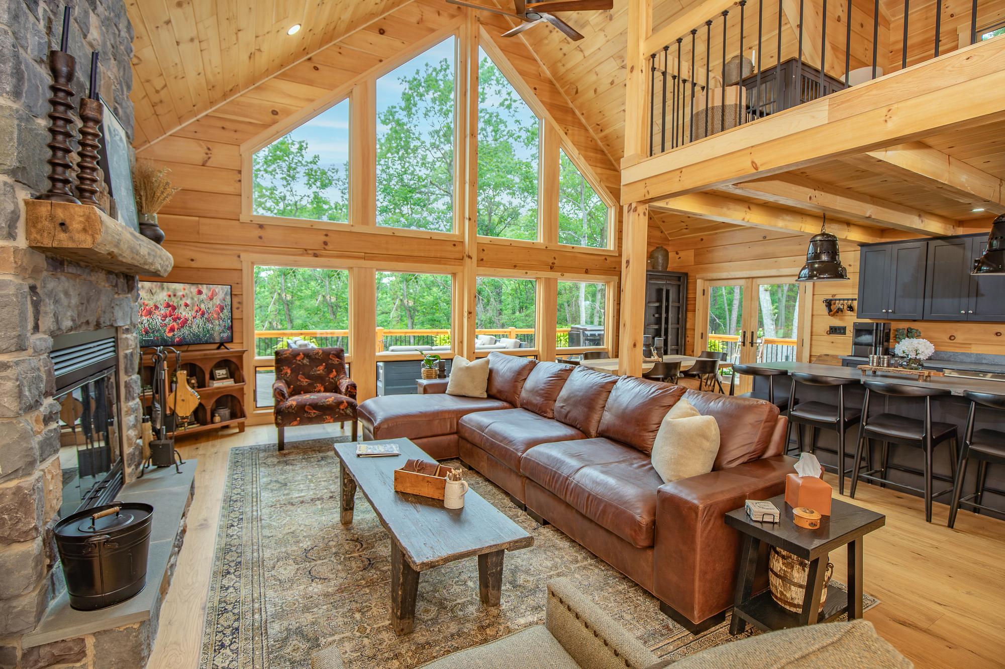 Great room with a floor-to-ceiling stone fireplace, leather sectional and a gable window wall of trees
