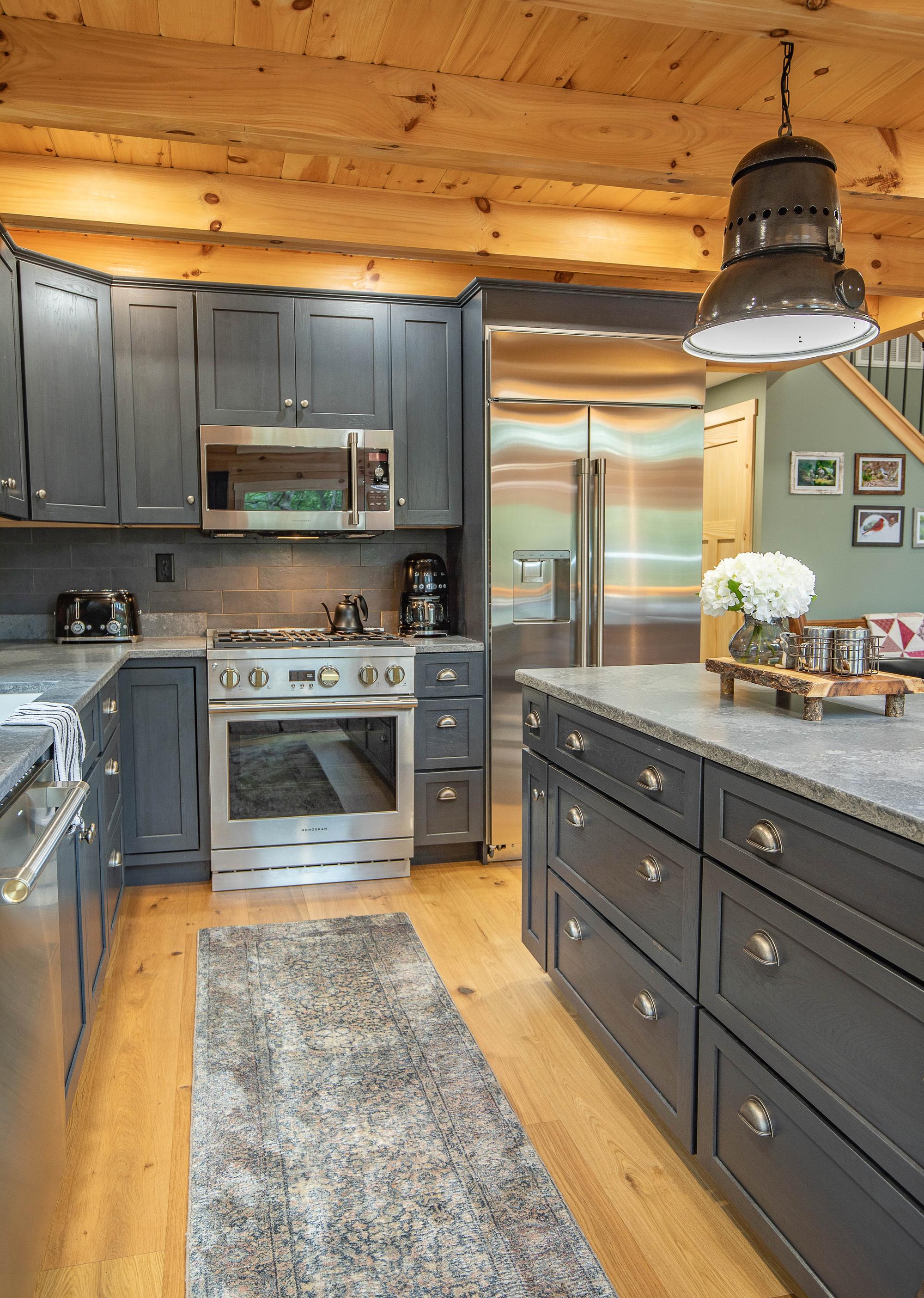 Kitchen range and stainless refrigerator in slate-blue cabinetry, a runner rug on the floor between the counters