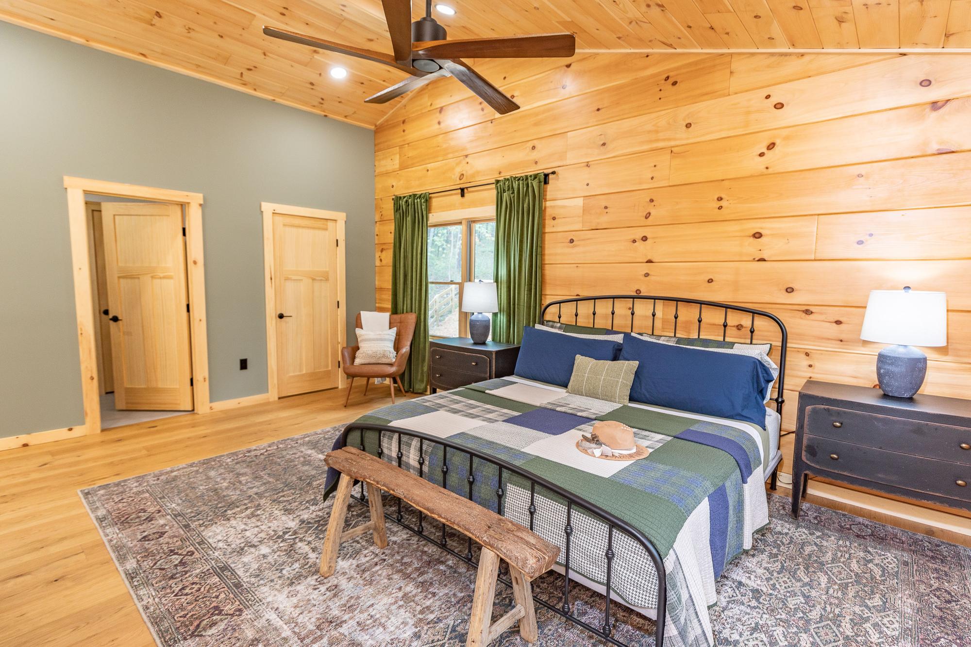 Main bedroom with a king bed, a sage accent wall and a rustic bench at its foot