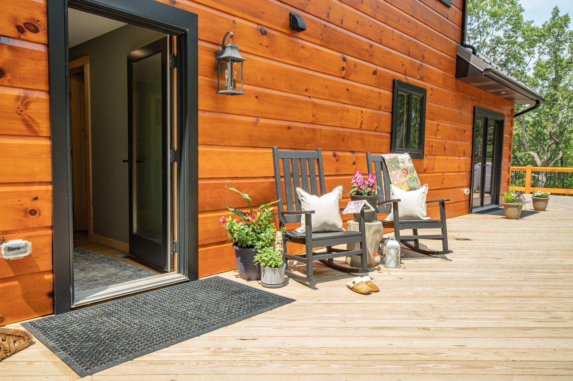 Side porch with rocking chairs and potted flowers beside an open front door