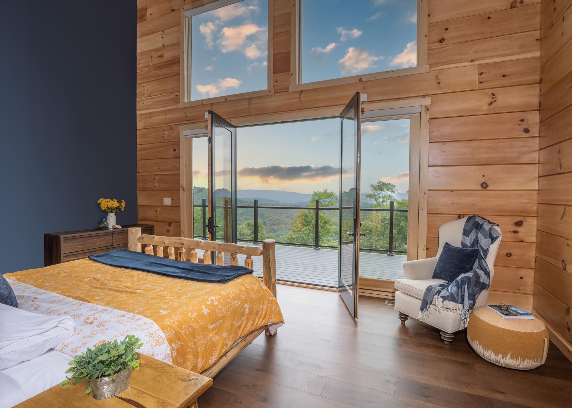 Main bedroom with a log bed and gold bedding, French doors standing open to the deck and the ridge at dusk