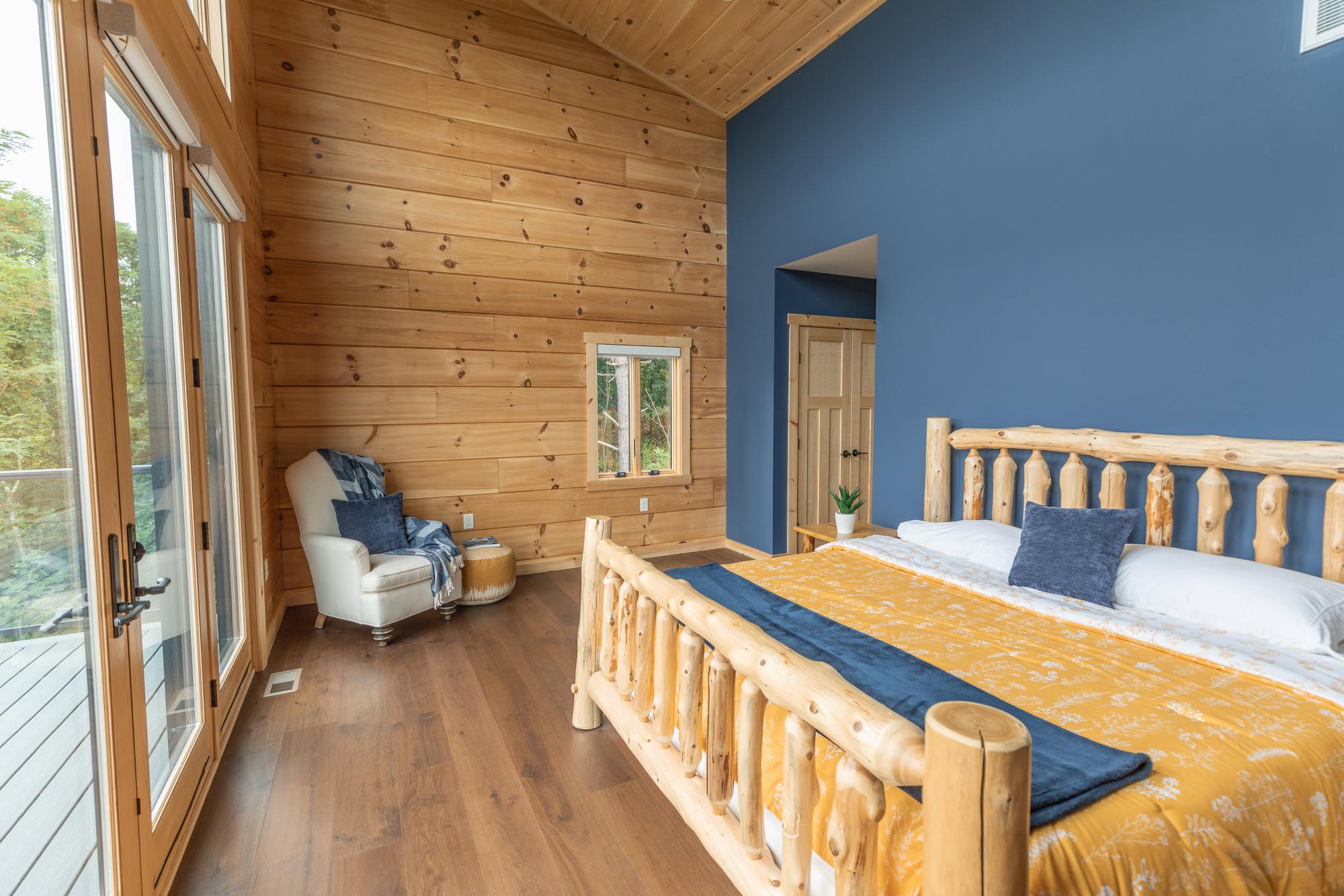 The main bedroom from the opposite corner, a navy accent wall behind the bed and doors to the deck