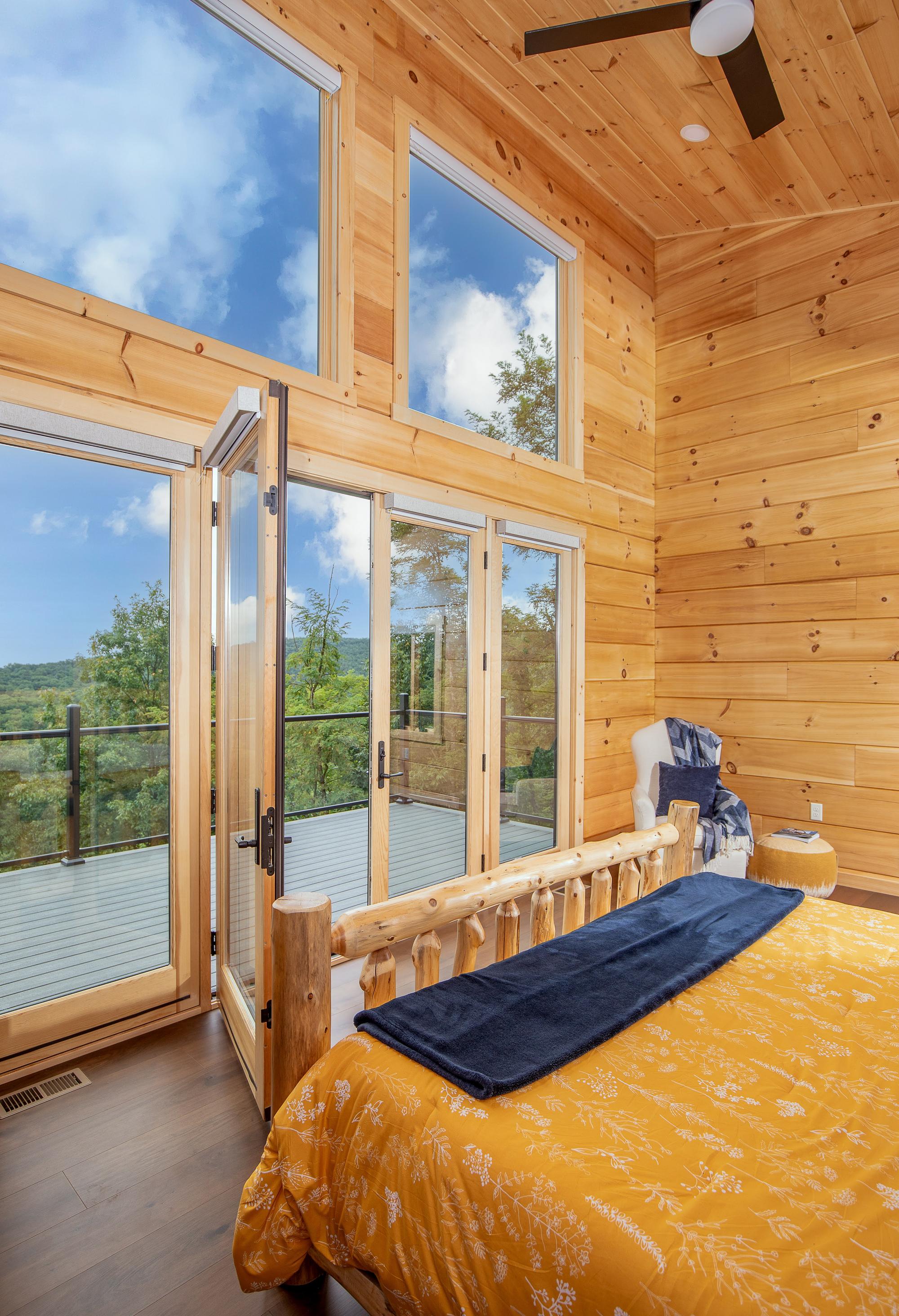 The bed and open deck doors from the foot of the bed, wood-paneled walls rising to a vaulted ceiling and one wall painted navy