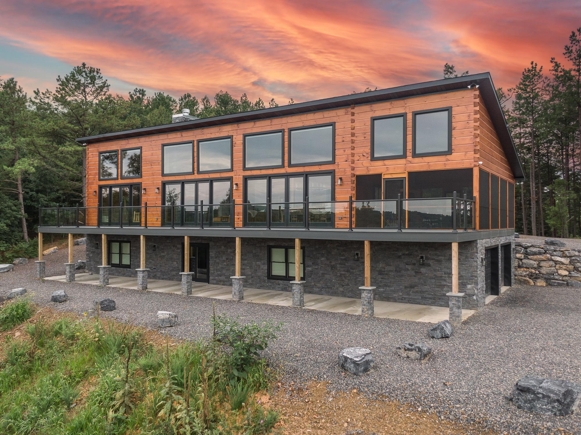 The home at sunset, log walls and glass railing beneath an orange sky