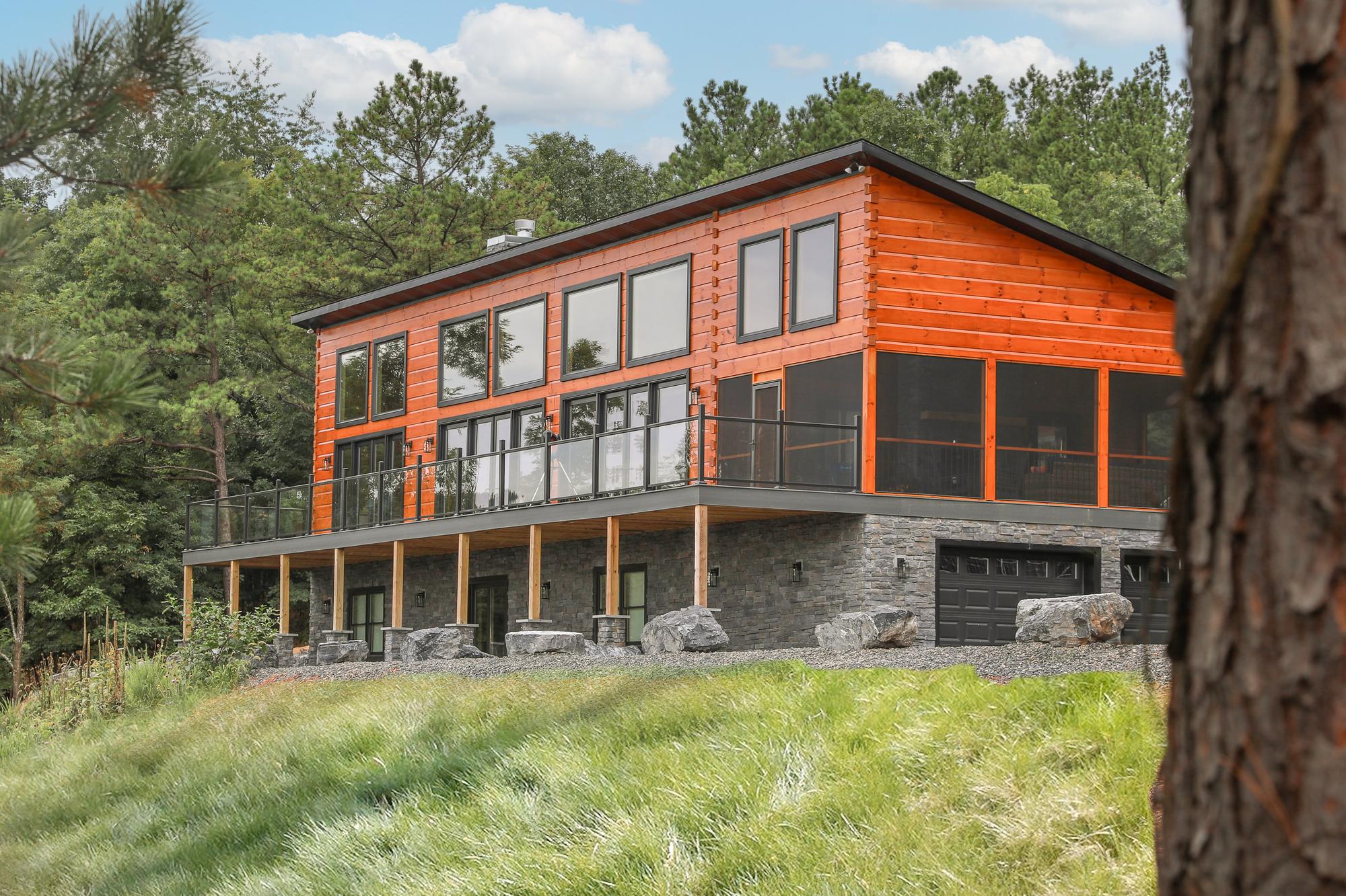 The home seen from the meadow below, log walls warm in late light above tall grass