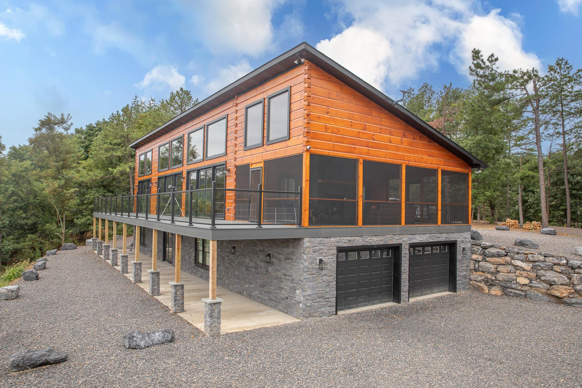 Three-quarter view from the drive, the deck carried on timber posts above a stone walkout with two garage bays