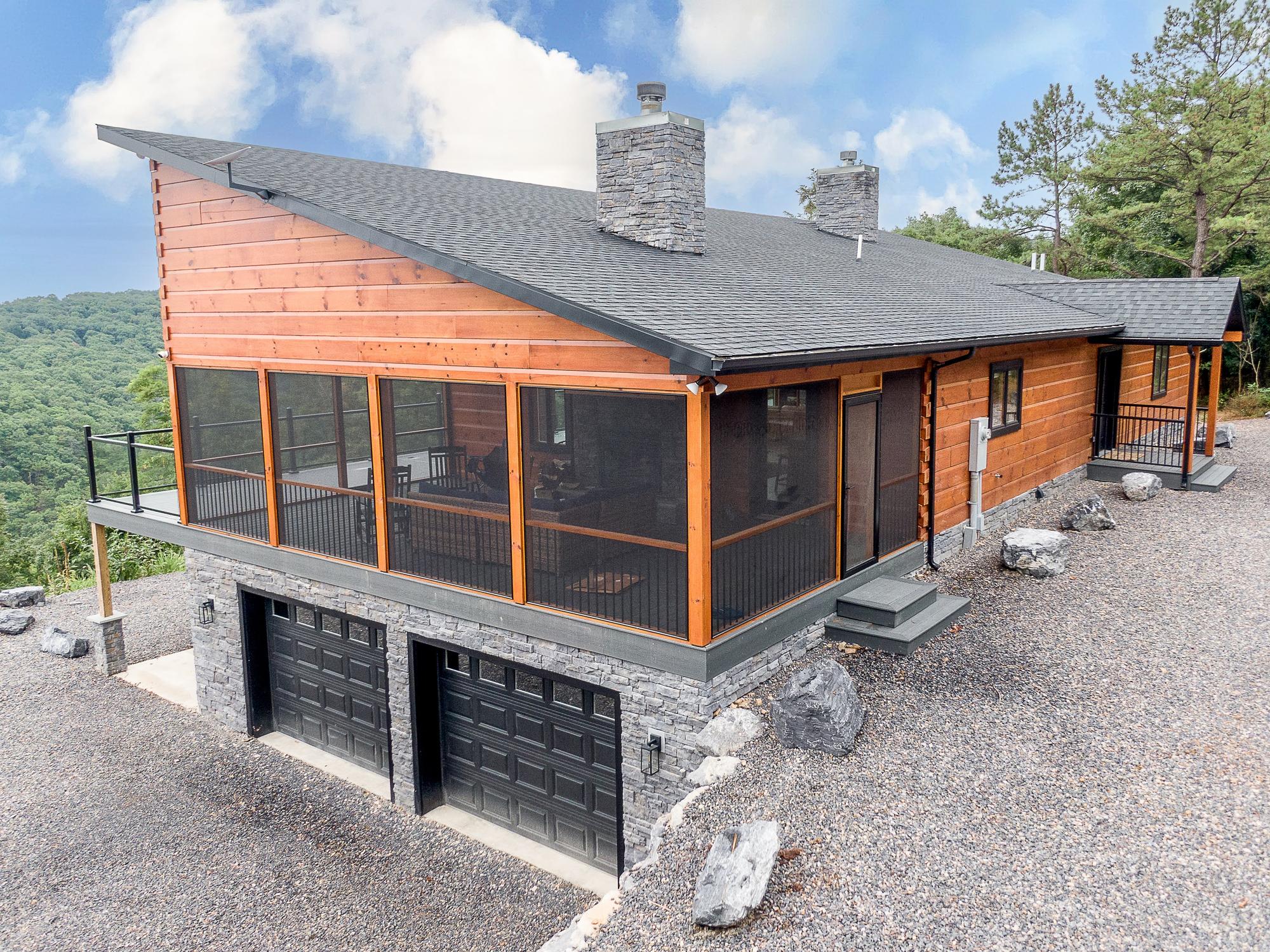 Elevated corner view showing the screened porch, two stone chimneys and garage doors set into the stone lower level